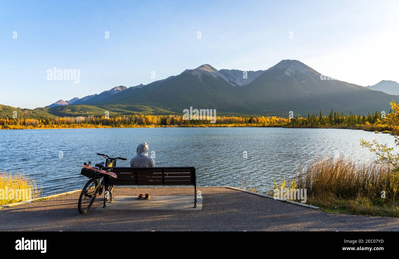 Touristen ruhen auf Holzbank, entspannen am Vermilion Lakes Seeufer im Herbst Laubsaison Sonnenuntergang Zeit. Radfahren im Banff National Park Stockfoto