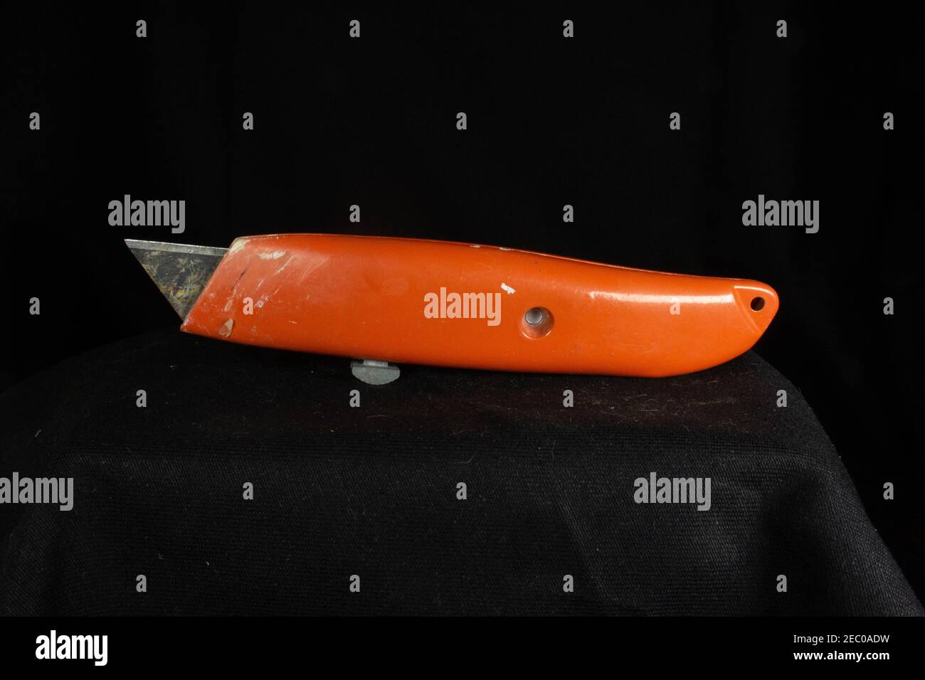 Schmutziges orangefarbenes Universalmesser mit ausgezeigter Klinge nach oben Isoliert auf schwarzem Hintergrund Stockfoto