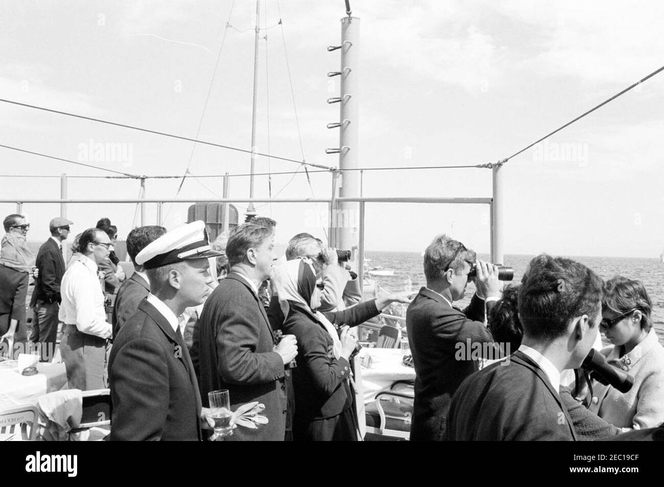 Präsident Kennedy beobachtet das 1st Americau0027s Cup Race. Präsident John F. Kennedy (rechts, Blick durch das Fernglas) und First Lady Jacqueline Kennedy (Mitte) beobachten das erste Rennen des Cup 1962 Americau0027s von Bord der USS Joseph P. Kennedy, Jr. auch im Bild: Stellvertretender Finanzminister, James A. Reed; Chef des Protokolls, Angier Biddle Duke; Botschafter von Großbritannien, Sir David Ormsby-Gore; Julia Ann Shepard (Frau des Naval Aide an den Präsidenten, Kapitän Tazewell Shepard); Skipper der Präsidentenyacht, u201cManitou,u201d Leutnant Charles Reid; Franklin D. Rooseve Stockfoto