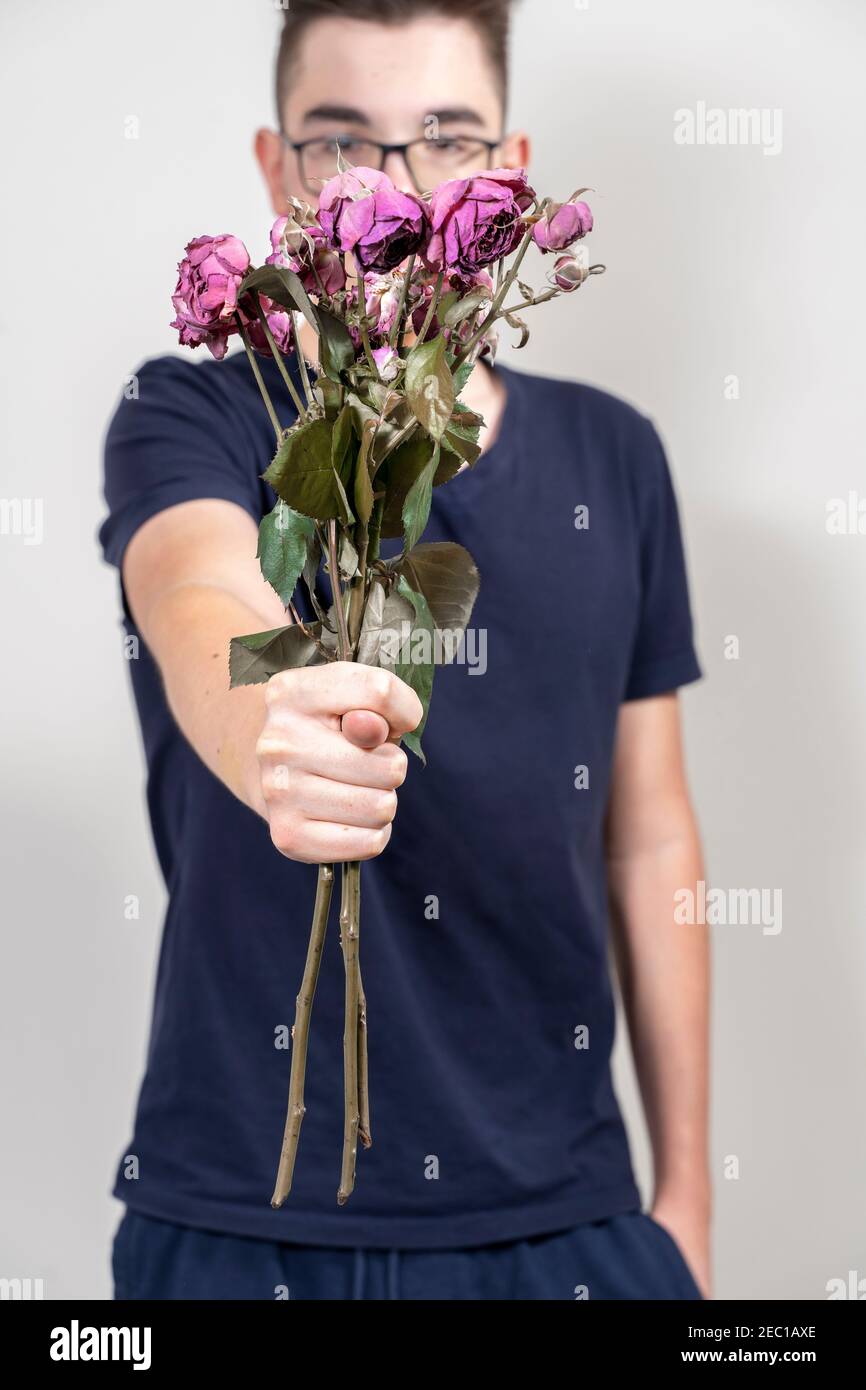 Junger Mann in Gläsern mit einem Strauß verwelkte Rosen und zeigt FEIGE. Unglückliche Liebe Konzept Stockfoto