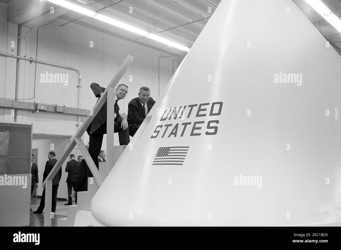 Besichtigung der NASA-Installationen: Houston, Texas, NASA Rich Building, Abfahrt, 11:10am Uhr. White House Secret Service Agent, Arthur L. u201cArtu201d Godfrey, hockt auf der Treppe, um ein Modell eines Apollo-Kommandomoduls zu sehen, während Präsident John F. Kennedyu0027s Besuch im Rich Building des bemannten Raumschiffszentrums, Houston, Texas; Mann, der mit Mr. Godfrey steht, ist nicht identifiziert. Präsident Kennedy besuchte das Zentrum im Rahmen einer zweitägigen Inspektionsreise durch die Feldinstallationen der National Aeronautics and Space Administration (NASA). Stockfoto