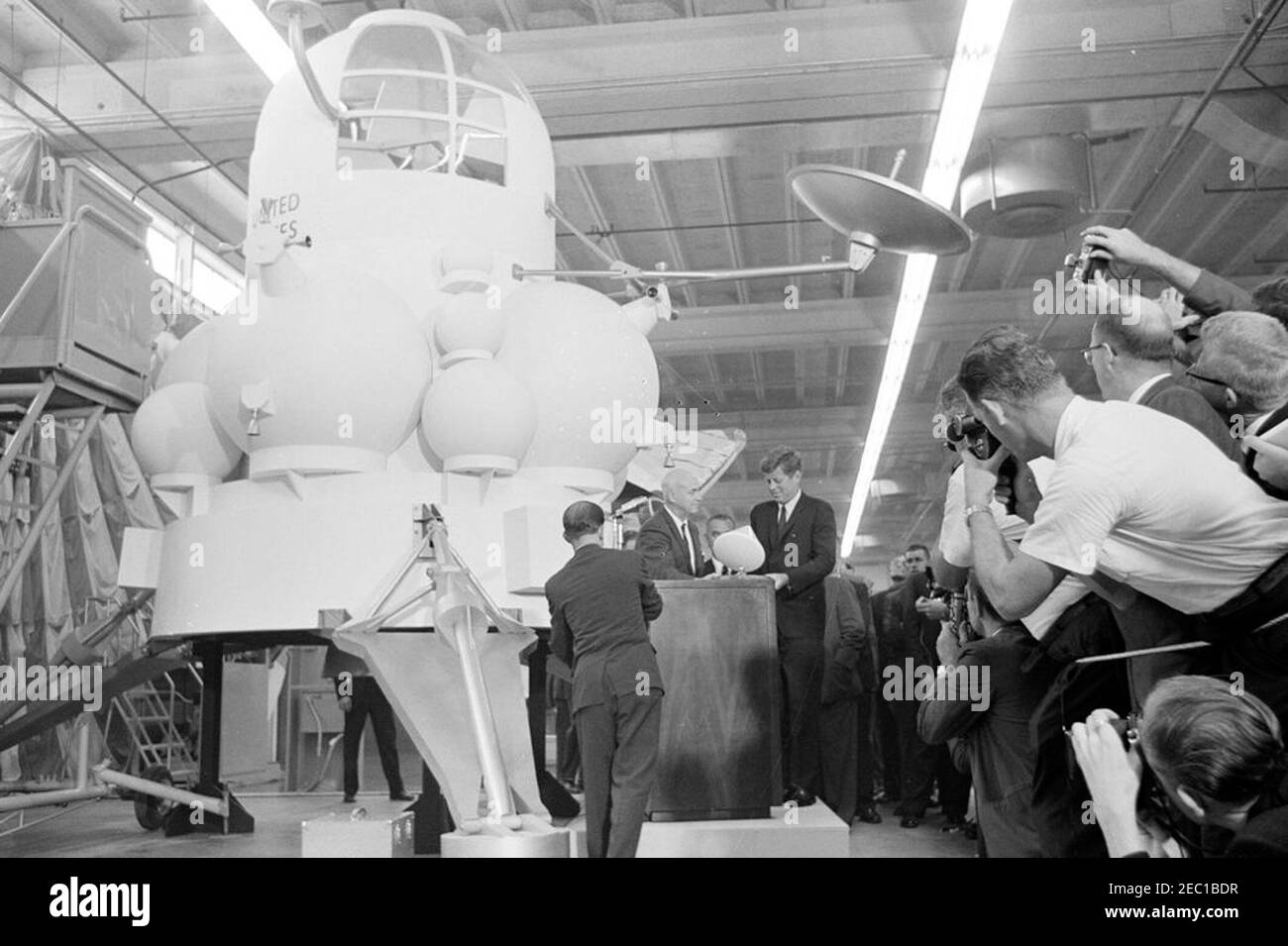 Besichtigung der NASA-Installationen: Houston, Texas, NASA Rich Building, Abfahrt, 11:10am Uhr. Präsident John F. Kennedy erhält ein maßstabsgetreues Modell des Apollo-Kommandomoduls vom Direktor des bemannten Raumschiffszentrums, Dr. Robert Gilruth (Mitte, am Rednerpult), nach einer Tour der Raumschiffsvorführungen in einem Hangar im Rich Building des bemannten Raumschiffszentrums, Houston, Texas; Ein Nachbau des Mondlanders (auch bekannt als u0022the Bugu0022) sitzt links im Hintergrund. Vice President Lyndon B. Johnson (teilweise versteckt) steht hinten, Fotografen beobachten rechts. Präsident Kennedy V Stockfoto