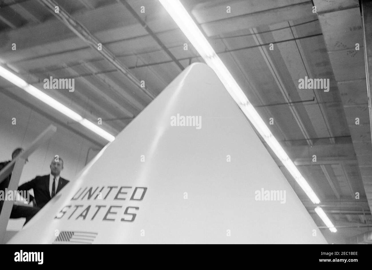 Besichtigung der NASA-Installationen: Houston, Texas, NASA Rich Building, Abfahrt, 11:10am Uhr. Blick auf den oberen Teil eines Apollo-Kommandomoduls, das während des Besuchs von Präsident John F. Kennedyu0027s im Rich Building des bemannten Raumschiffszentrums, Houston, Texas, ausgestellt wurde; links steht der Geheimagent des Weißen Hauses, Arthur L. u201cArtu201d Godfrey (teilweise versteckt). Präsident Kennedy besuchte das Zentrum im Rahmen einer zweitägigen Inspektionsreise durch die Feldinstallationen der National Aeronautics and Space Administration (NASA). [Unschärfe im Bild ist ursprünglich negativ.] Stockfoto
