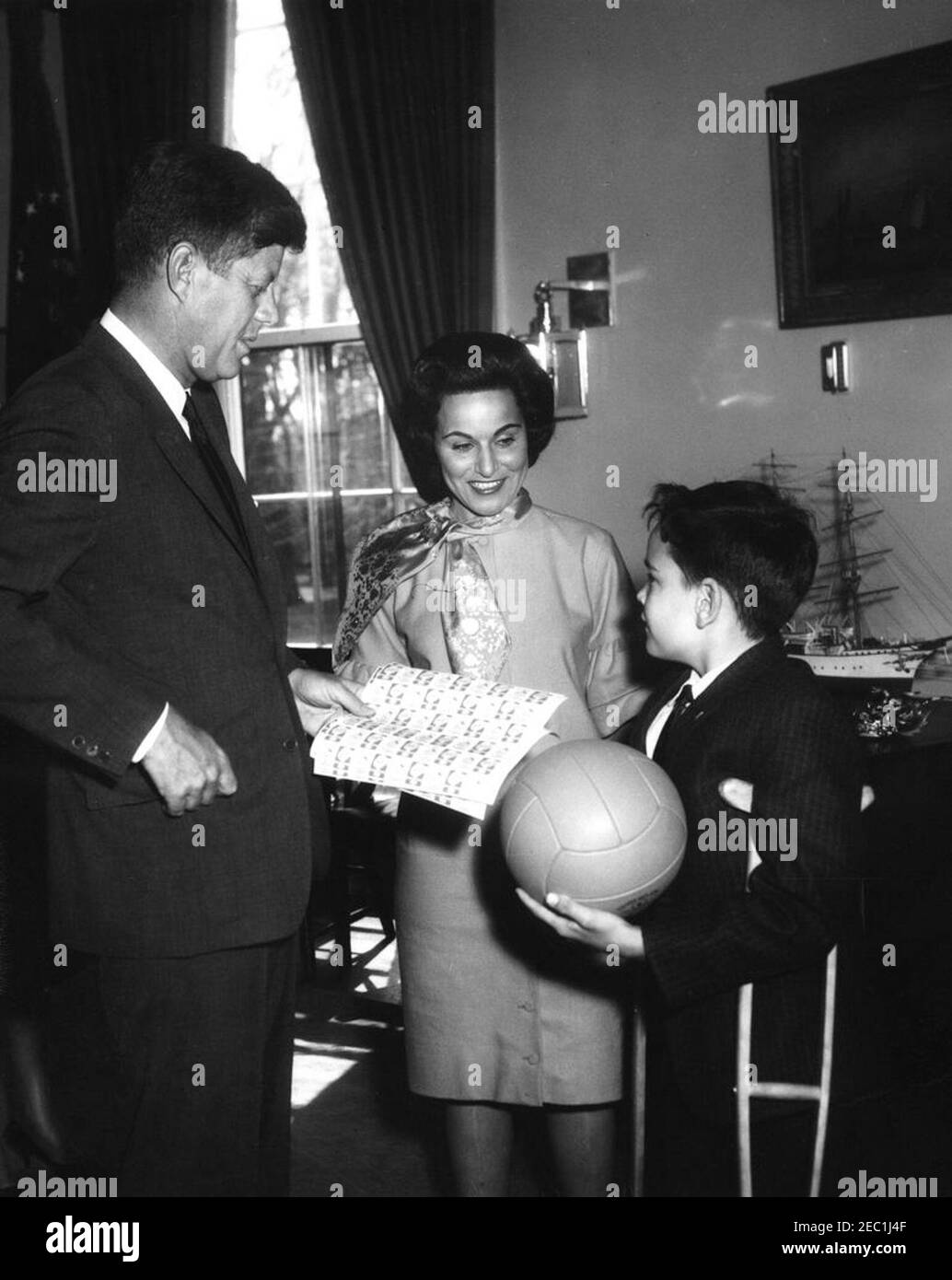 Besuch von Thomas A. Doyle, III, 1962 Ostersiegelkind, 12:07pm. Thomas A. Doyle, III (rechts), das 1962 Ostersiegelkind, überreicht Präsident John F. Kennedy mit Blättern von 1962 Ostersiegeln. Im Zentrum steht Pauline Phillips (Zeitungskolumnistin Abigail Van Buren, oder u201cDear Abbyu201d), Vorsitzende des Easter Seal Drive, gesponsert von der National Society for Crippled Children and Adults. Oval Office, White House, Washington, D.C. Stockfoto