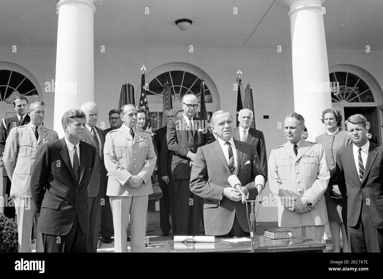 Vereidigung, General Maxwell Taylor, Chairman, JCS, 12:00pm Uhr. Der stellvertretende Verteidigungsminister Roswell Gilpatric (Mitte rechts, bei Mikrofonen) hält während der Vereidigung von General Maxwell D. Taylor als Vorsitzender der Joint Chiefs of Staff (JCS) eine Rede. Präsident John F. Kennedy beobachtet von links; General Taylor und Generalstaatsanwalt Robert F. Kennedy stehen rechts. Blick von den Stufen der West Wing Colonnade, beginnend ganz hinten (von links nach rechts): Marine Aide an den Präsidenten, Kapitän Tazewell T. Shepard, Jr.; Military Aide an den Präsidenten, General Chester V. Stockfoto