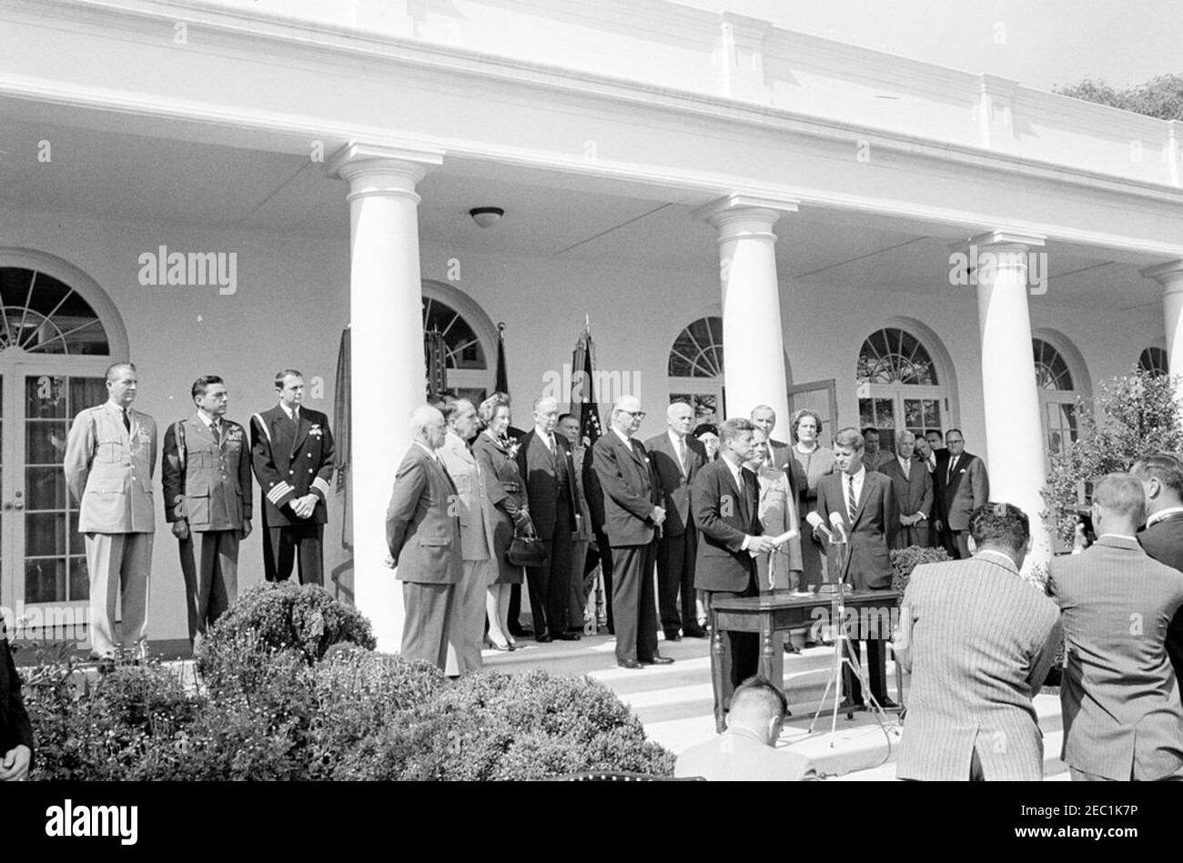 Vereidigung, General Maxwell Taylor, Chairman, JCS, 12:00pm Uhr. Präsident John F. Kennedy (Mitte rechts, an Mikrofonen) hält Bemerkungen während der Vereidigung von General Maxwell D. Taylor als Vorsitzender der Joint Chiefs of Staff (JCS); General Taylor und Generalstaatsanwalt Robert F. Kennedy stehen rechts von Präsident Kennedy. Blick von den Stufen der West Wing Colonnade, beginnend ganz links (links nach rechts): Military Aide an den Präsidenten, General Chester V. Clifton; Air Force Aide an den Präsidenten, Brigadier General Godfrey T. McHugh; Naval Aide an den Präsidenten, Kapitän Stockfoto