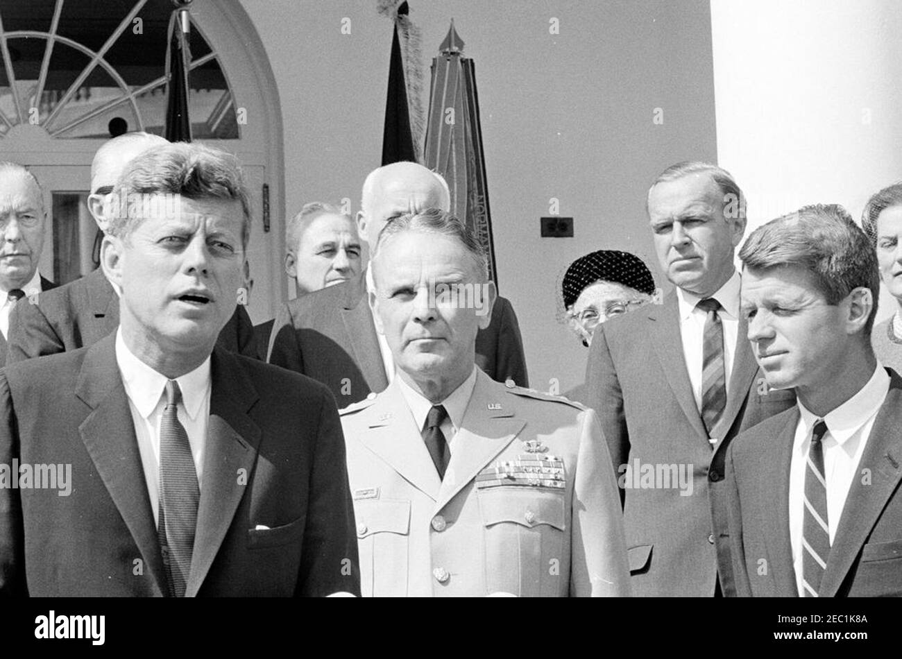 Vereidigung, General Maxwell Taylor, Chairman, JCS, 12:00pm Uhr. Präsident John F. Kennedy (links) hält während der Vereidigung von General Maxwell D. Taylor als Chairman of the Joint Chiefs of Staff (JCS) eine Rede. Im Blick, ganz hinten beginnend (von links nach rechts): Admiral Arthur W. Radford; Navy-Sekretär Fred Korth (meist versteckt); General Nathan F. Twining; Sekretär der Luftwaffe, Eugene M. Zuckert (teilweise versteckt); General Taylor; Pearle Davenport Taylor (hinten, teilweise versteckt); Stellvertretender Verteidigungsminister, Roswell Gilpatric; Generalstaatsanwalt, Robert F. Ke Stockfoto