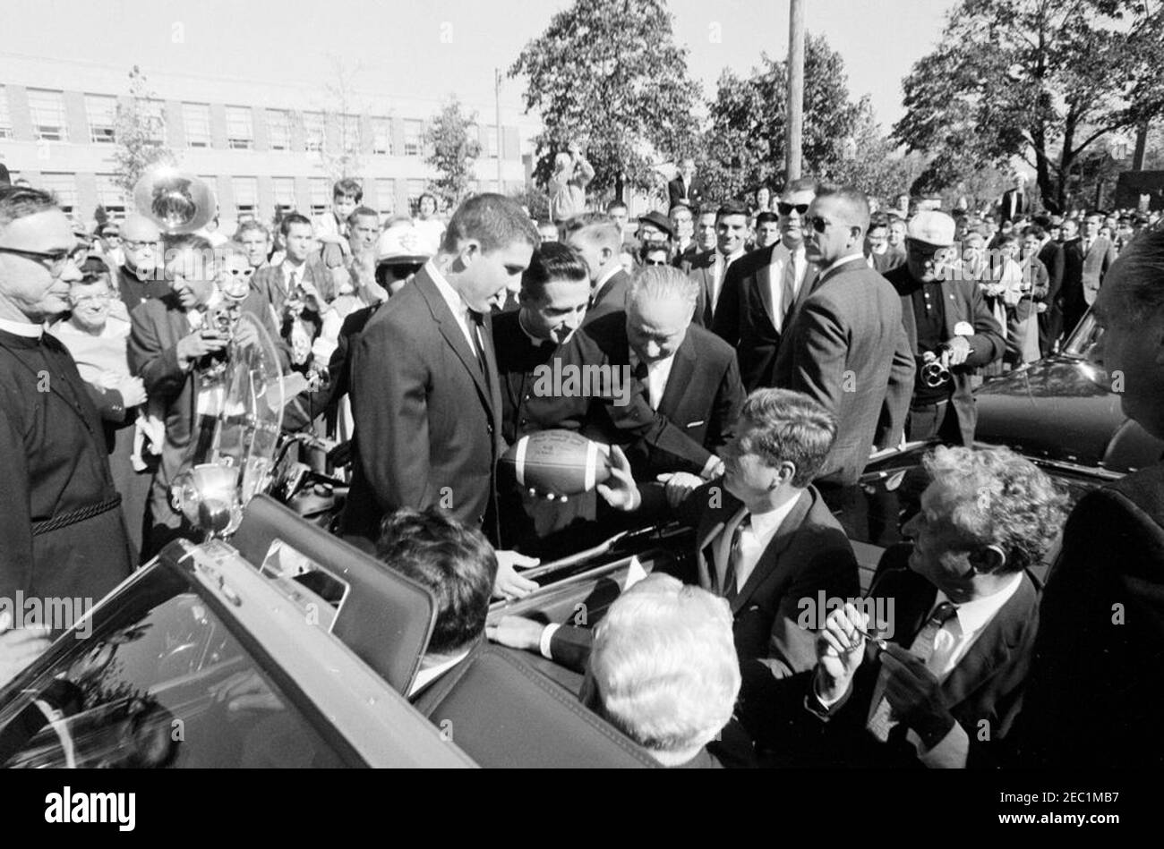 Kongreßfeldzug Reise: Cleveland, Ohio, Ankunft, Rallye, Autokolonne, Abfahrt. Präsident John F. Kennedyu2019s Autokolonne hält vor der St. Edward High School in Lakewood, Ohio, während einer Kongresskampagne Reise; Präsident Kennedy erhält einen Fußball im Namen der Studentenschaft von Senior Class Präsident Robert Cutter, und Rektor, Bruder Charles Krupp. Ebenfalls abgebildet: Repräsentant Michael J. Feighan aus Ohio (im Vordersitz des Cabrios, Rücken zur Kamera); Senator Frank Lausche aus Ohio (auf dem Rücksitz mit Präsident Kennedy); Gouverneur von Ohio, Michael V. DiSalle (stehend bei f Stockfoto