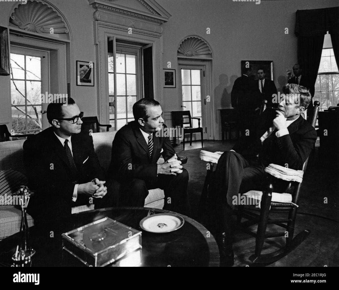 Treffen mit dem Außenminister von Costa Rica, Daniel Oduber Quiru00f3s, 11:20am Uhr. Präsident John F. Kennedy (im Schaukelstuhl) trifft sich mit Außenminister von Costa Rica, Daniel Oduber Quiru00f3s. Ganz links sitzt der Botschafter von Costa Rica, Gonzalo J. Facio Segreda. Im Hintergrund sprechen der Sonderassistent des Präsidenten, Ralph Dungan (Mitte), und der US-Chef des Protokolls, Angier Biddle Duke (rechts), mit einem unbekannten Mann. Oval Office, White House, Washington, D.C. Stockfoto