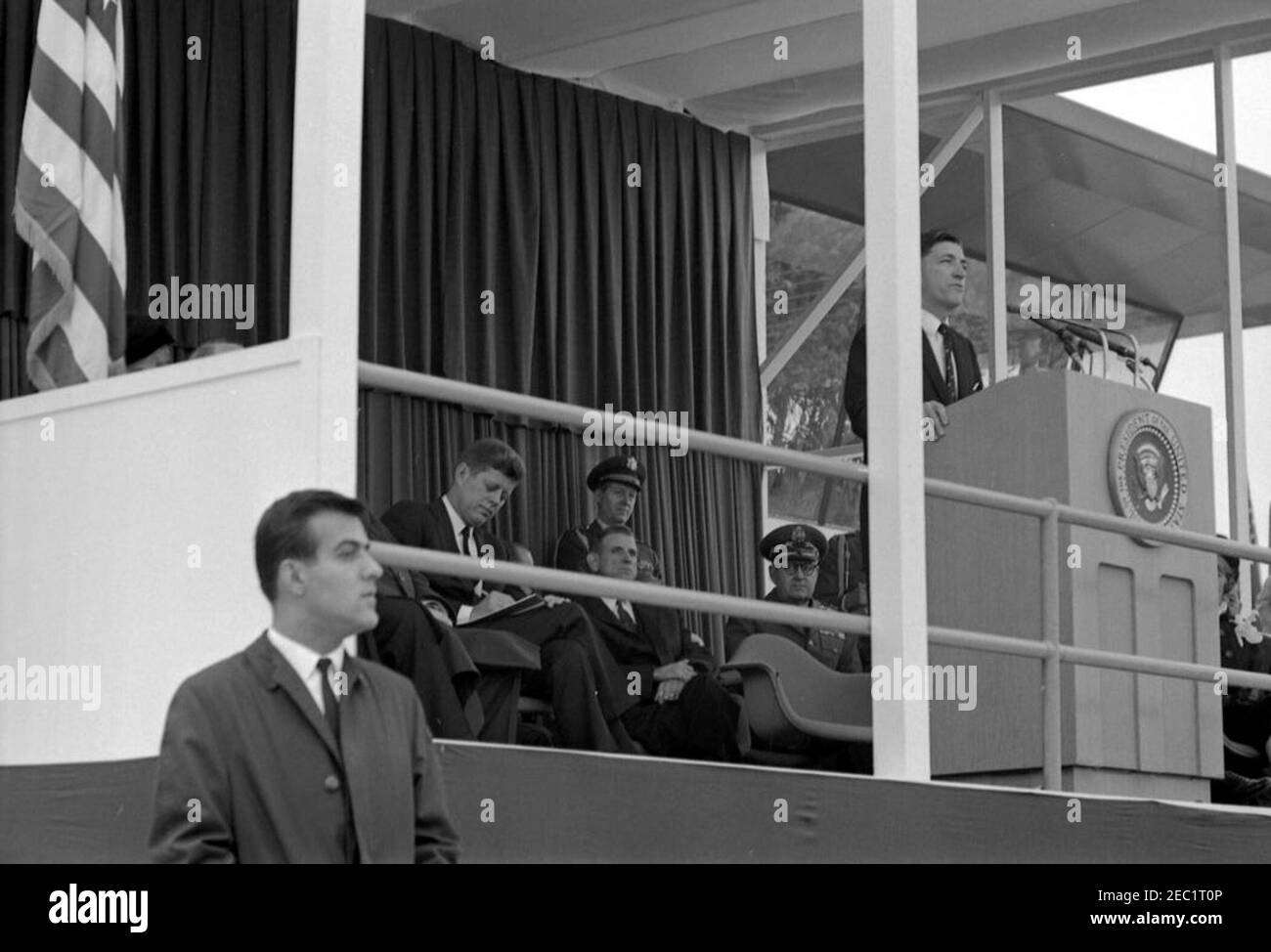 Dedication Ceremonies, Dulles International Airport, 11:12am Uhr. Der Administrator der Federal Aviation Agency (FAA), Najeeb Halaby (am Rednerpult), hält bei der Einweihungszeremonie für den internationalen Flughafen Dulles, benannt nach dem verstorbenen Außenminister John Foster Dulles, Bemerkungen; Präsident John F. Kennedy (schriftlich) sitzt in der Mitte links. Ebenfalls auf der Plattform von speakersu0027 abgebildet: Vertreter Oren Harris (Arkansas); Militärhilfe an den Präsidenten, General Chester V. Clifton (stehend); Stabschef der United States Air Force, General Curtis E. LeMay. Geheimagent des Weißen Hauses, Ken Stockfoto