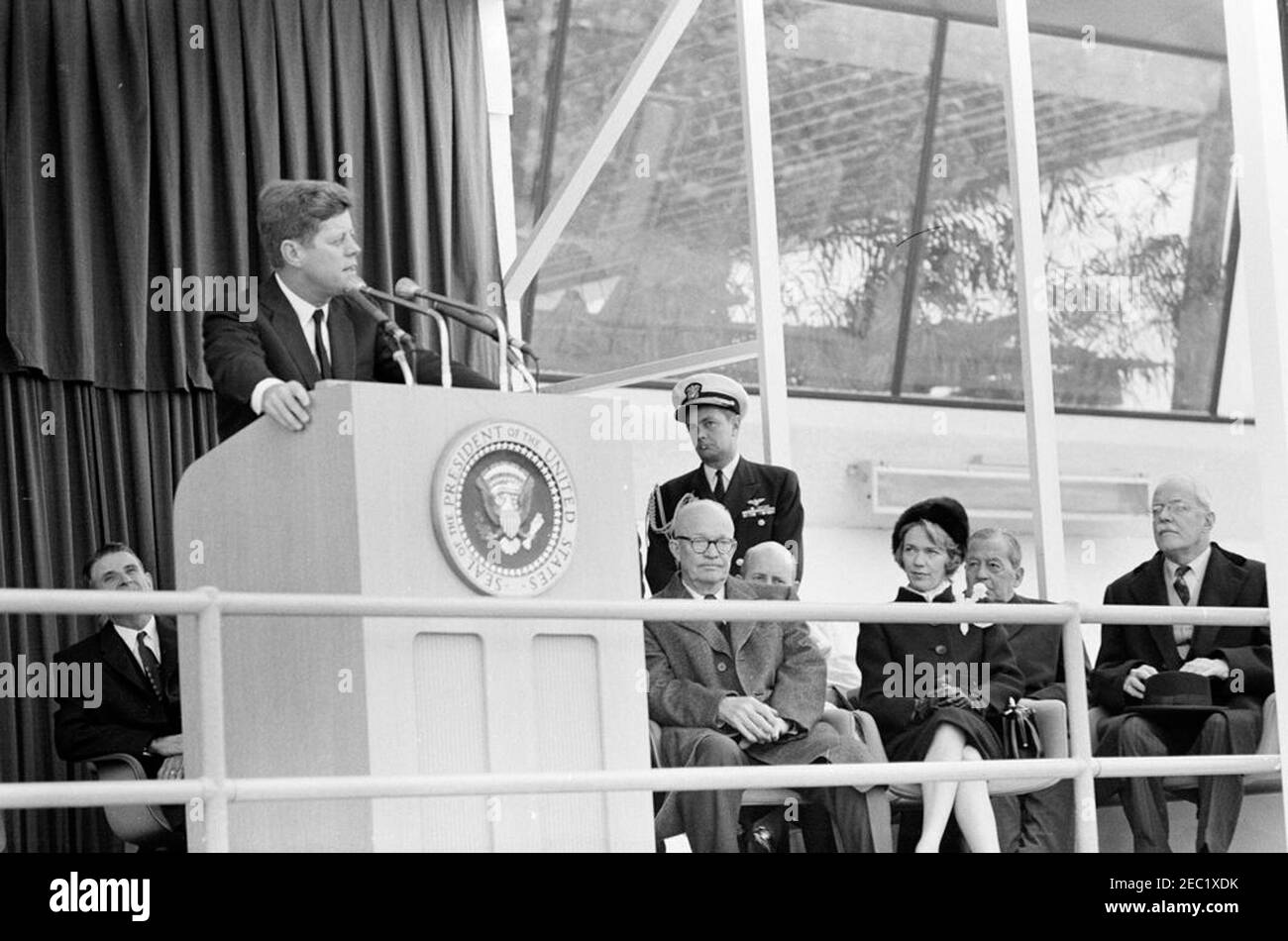 Dedication Ceremonies, Dulles International Airport, 11:12am Uhr. Präsident John F. Kennedy (auf dem Rednerpult) hält Bemerkungen bei der Einweihungszeremonie für den internationalen Flughafen Dulles, benannt nach dem verstorbenen Staatssekretär John Foster Dulles. Ebenfalls auf der Plattform speakersu2019 abgebildet: Vertreter Oren Harris von Arkansas (hinter Rednerpult); ehemaliger Präsident, General Dwight D. Eisenhower; Naval Aide to the President, Captain Tazewell T. Shepard, Jr. (stehend); Aline B. Saarinen (Witwe des Architekten für den Flughafen, Eero Saarinen); ehemaliger Direktor der Central Intelligence Agency (CIA), Allen Stockfoto