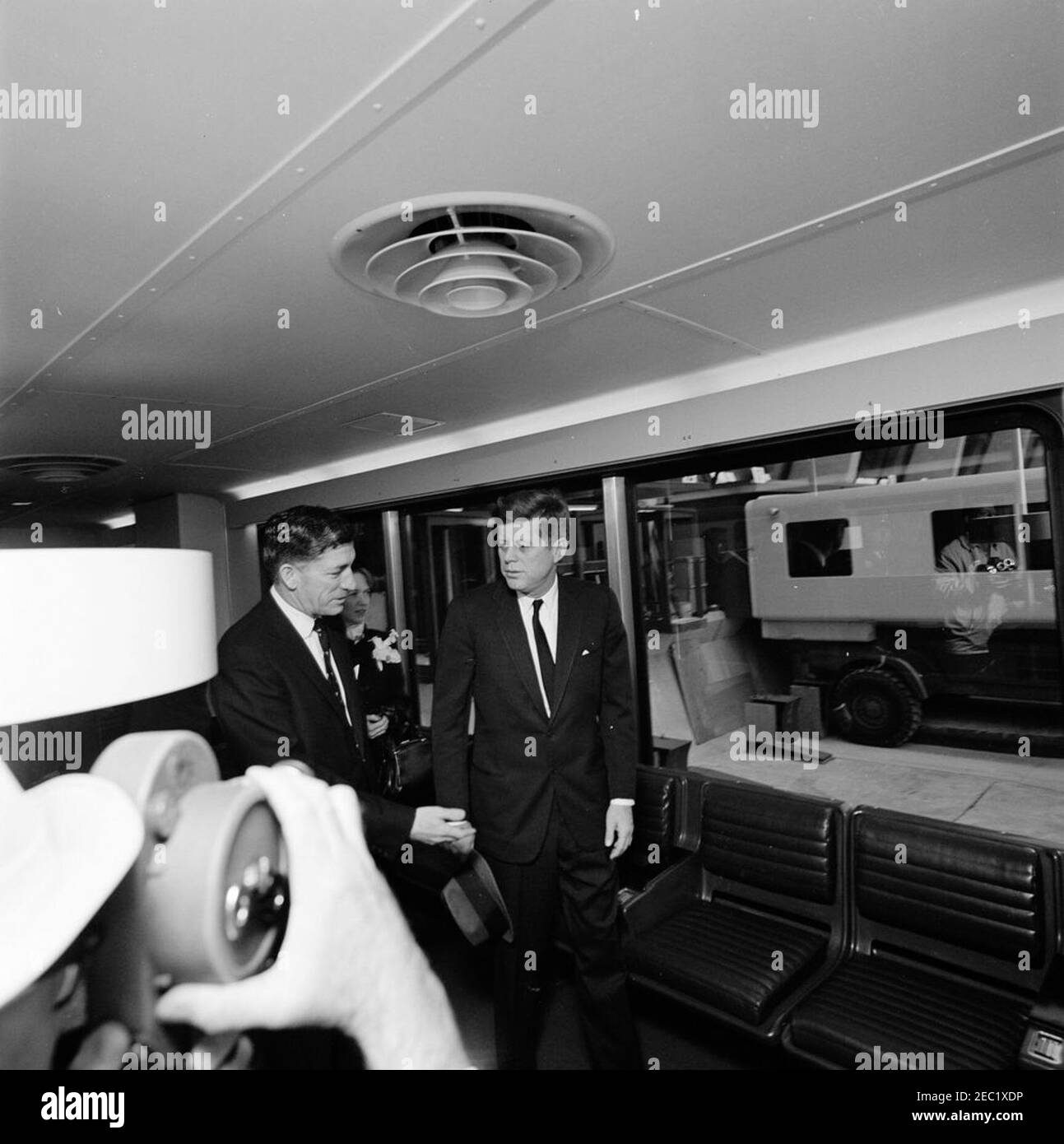 Dedication Ceremonies, Dulles International Airport, 11:12am Uhr. Präsident John F. Kennedy (Mitte, mit Hut) geht durch eine der mobilen Lounges am internationalen Flughafen Dulles, während der Einweihungszeremonie für den Flughafen, der nach dem verstorbenen Außenminister John Foster Dulles benannt wurde. Der Verwalter des Luftfahrtbundesamtes (FAA), Najeeb Halaby, geht nach links; Aline B. Saarinen (Witwe des Architekten für den Flughafen, Eero Saarinen) folgt nach hinten. Chantilly, Virginia. Stockfoto