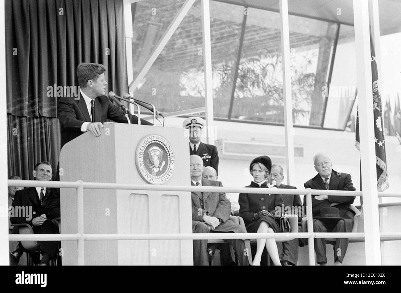 Dedication Ceremonies, Dulles International Airport, 11:12am Uhr. Präsident John F. Kennedy (auf dem Rednerpult) hält Bemerkungen bei der Einweihungszeremonie für den internationalen Flughafen Dulles, benannt nach dem verstorbenen Staatssekretär John Foster Dulles. Ebenfalls auf der Plattform speakersu2019 abgebildet: Vertreter Oren Harris von Arkansas (hinter Rednerpult); ehemaliger Präsident, General Dwight D. Eisenhower; Naval Aide to the President, Captain Tazewell T. Shepard, Jr. (stehend); Aline B. Saarinen (Witwe des Architekten für den Flughafen, Eero Saarinen); ehemaliger Direktor der Central Intelligence Agency (CIA), Allen Stockfoto