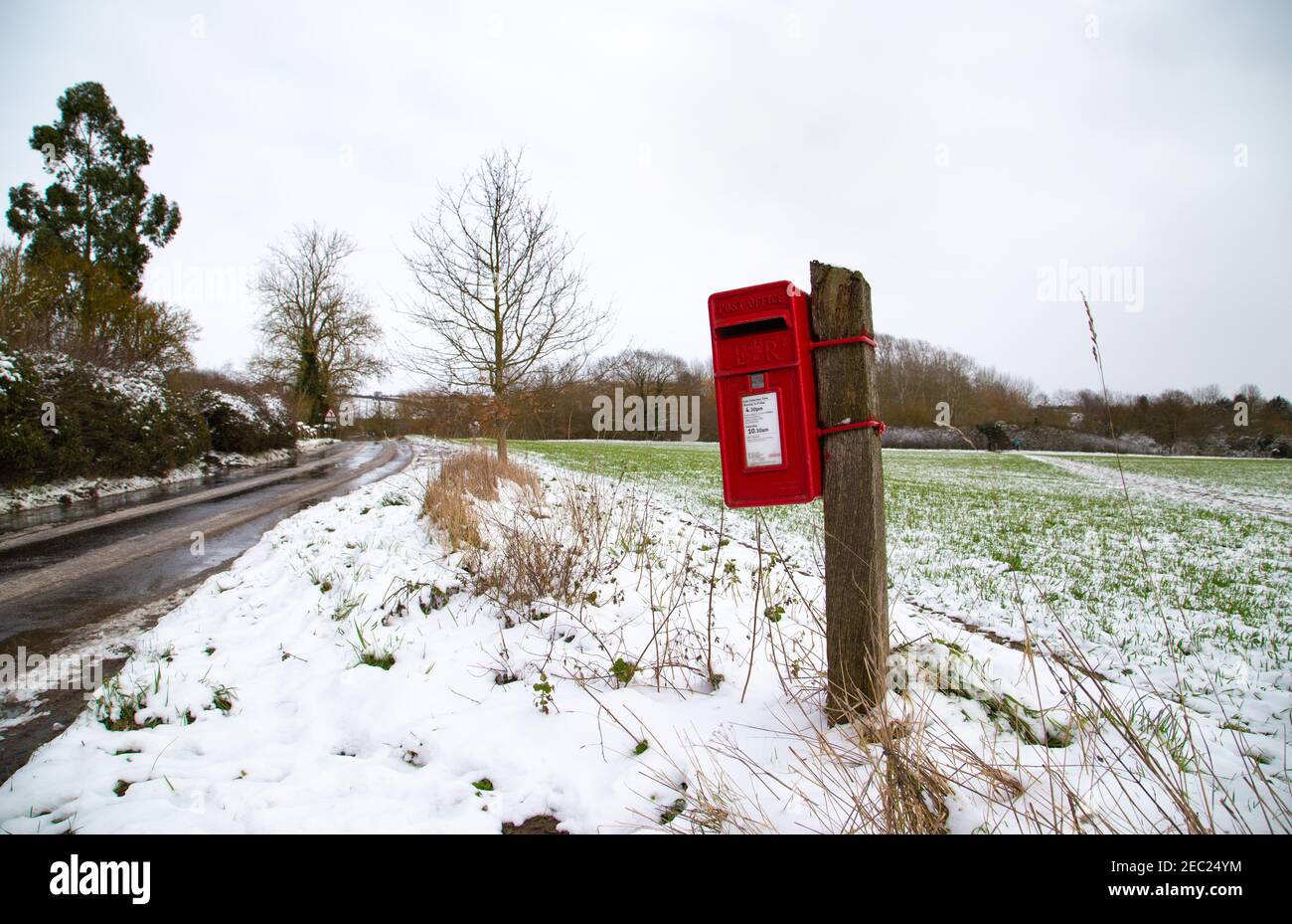 Roter britischer Briefkasten, Winterzeit. Pole montiert englischen Briefkasten auf dem Land. Winter, verschneite Tage Stockfoto