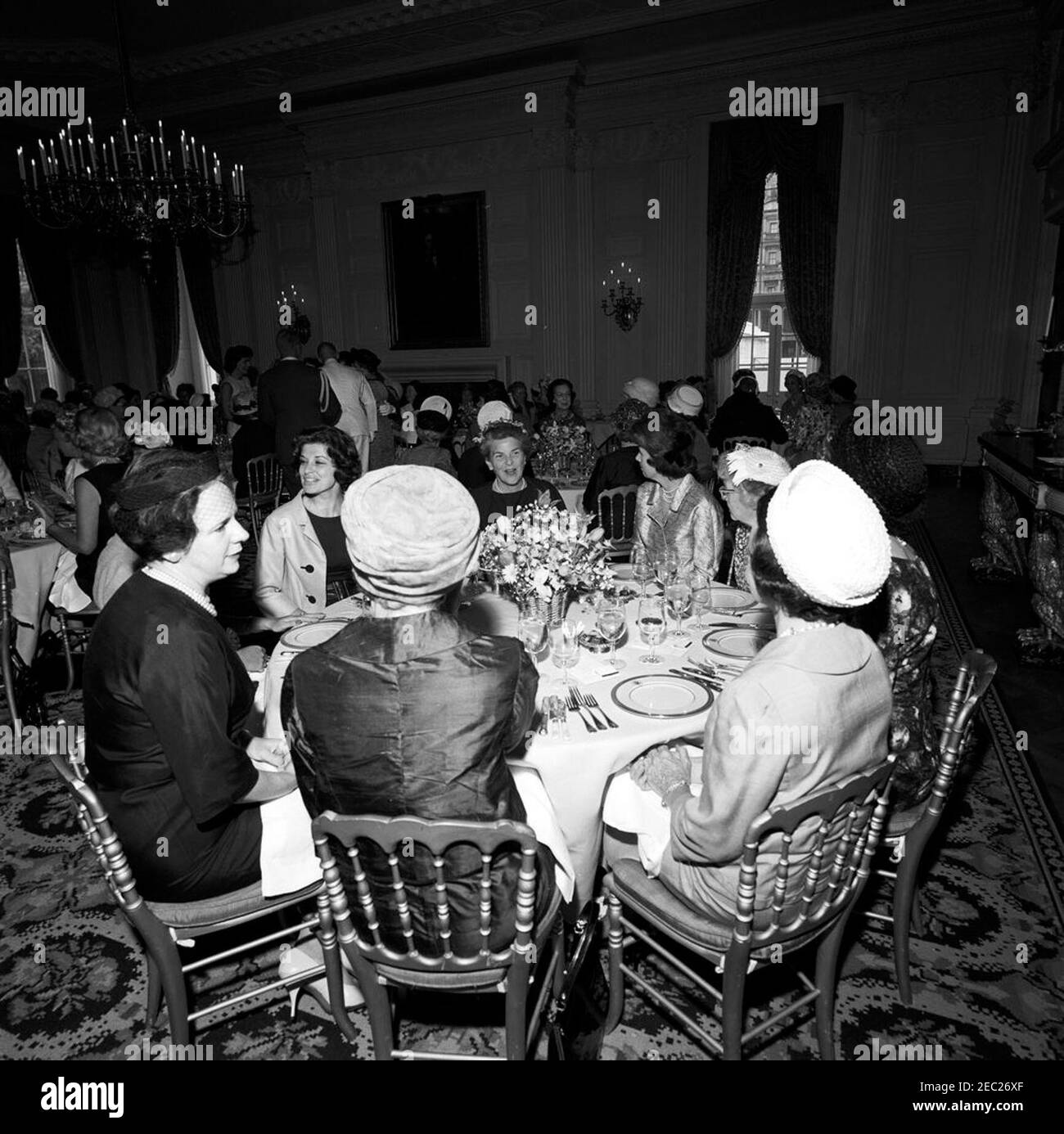 First Lady Jacqueline Kennedyu0027s (JBK) Mittagessen für Senatorsu0027 Ehefrauen. First Lady Jacqueline Kennedy (links im Hintergrund) nimmt an einem Mittagessen für senatorsu2019 Ehefrauen im State Dining Room des Weißen Hauses, Washington, D.C., Teil.zu den Sitzen am Tisch im Vordergrund gehören: Die ehemalige Vertreterin Emily Taft Douglas (Ehefrau von Senator Paul H. Douglas aus Illinois); Phyllis Ellsworth Dillon (Ehefrau von Secretary of the Treasury, C. Douglas Dillon). Ebenfalls abgebildet (im Hintergrund): Lorraine Cooper (Ehefrau von Senator John Sherman Cooper aus Kentucky); Senatorin Maurine Neuberger aus Oregon (teilweise versteckt Stockfoto