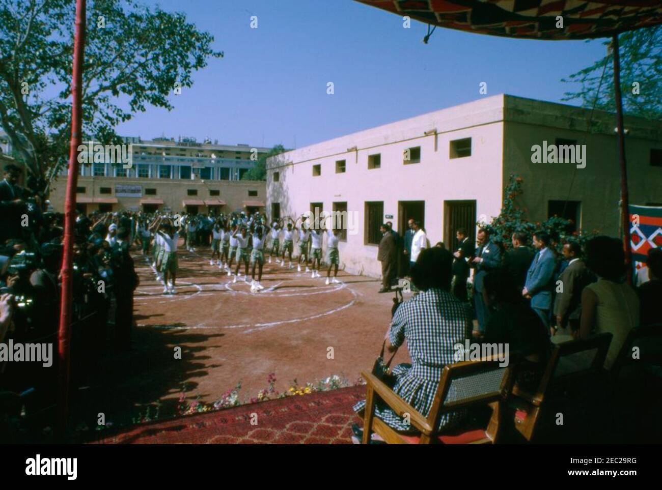 First Lady Jacqueline Kennedyu2019s (JBK) Reise nach Indien und Pakistan: New Delhi, Delhi, Indien, Besuch in Bal Sahyog, Organisation für bedürftige Kinder. First Lady Jacqueline Kennedy (ganz rechts, im Schatten) sieht einer Gruppe von Kindern bei ihrem Besuch in Bal Sahyog, einer sozialen Organisation für bedürftige Kinder, beim Tanz zu. Neu Delhi, Indien. Stockfoto