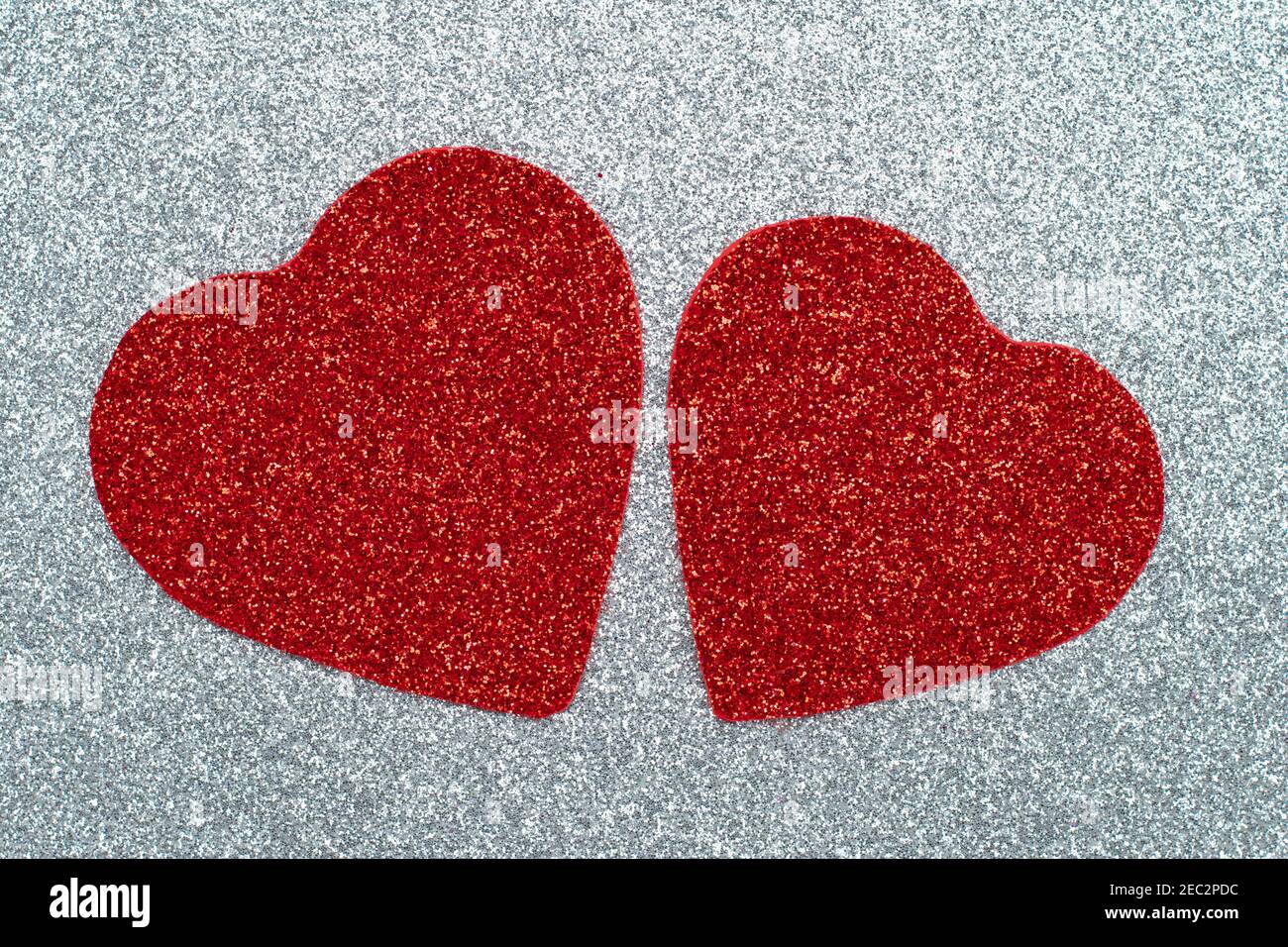 Zwei geschnitzte rote Herzen auf einem grauen glänzenden Hintergrund. Abstrakt glänzendes Muster. Bastelpapier, Glitzer, funkelnde Textur. Liebeskonzept Stockfoto