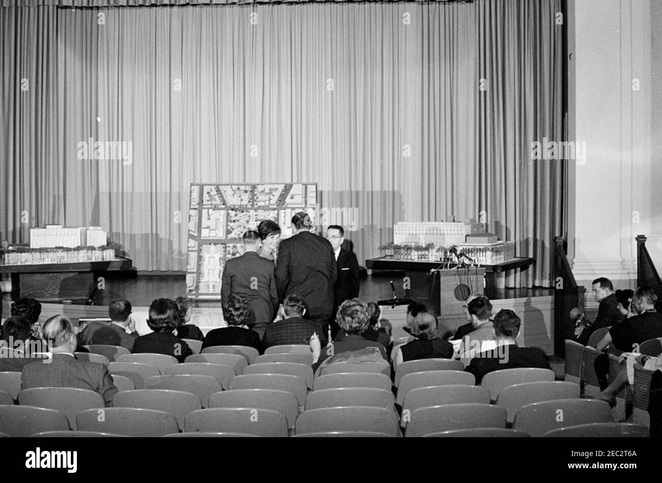 First Lady Jacqueline Kennedy (JBK) nimmt an der Enthüllung der Wiederaufbaupläne des Lafayette Square Teil. First Lady Jacqueline Kennedy nimmt an einer Presseinterpremiere der historischen Bewahrung und der Umbaupläne für Lafayette Square, Washington, D.C. Teil.Mrs. Kennedy (im Hintergrund) besucht den Architekten des Lafayette Square Umbauplanung, John Carl Warnecke (Mitte, zurück zur Kamera), und den Administrator der General Services Administration (GSA), Bernard L. Boutin. GSA Building Auditorium, Washington, D.C. Stockfoto