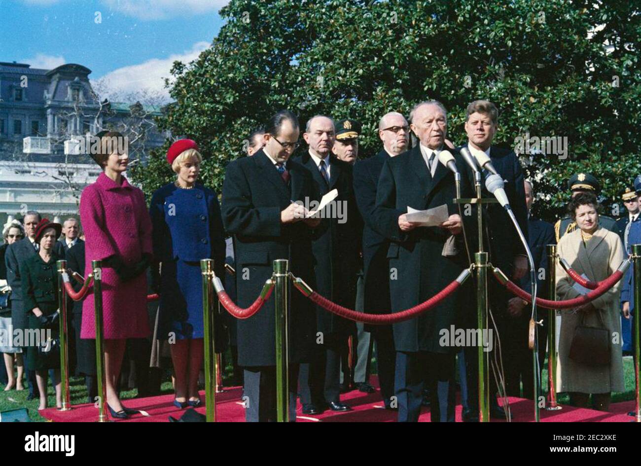 Ankunftszeremonie für Konrad Adenauer, Bundeskanzler der Bundesrepublik Deutschland, 10:45am Uhr. Bundeskanzler Dr. Konrad Adenauer (an Mikrofonen) hält bei den Ankunftszeremonien zu seinen Ehren eine Rede. Auf der Überprüfungsplattform: Präsident John F. Kennedy; First Lady Jacqueline Kennedy; Libeth Werhahn, Tochter von Bundeskanzler Adenauer; Dolmetscher für das deutsche Außenministerium, Heinz Weber; US-Außenminister Dean Rusk; Vorsitzender der Generalstabschefs, General Maxwell D. Taylor; Botschafter der Bundesrepublik Deutschland, Karl Heinrich Knappstein. Auch im Bild: Assistant Chief of Language Serv Stockfoto