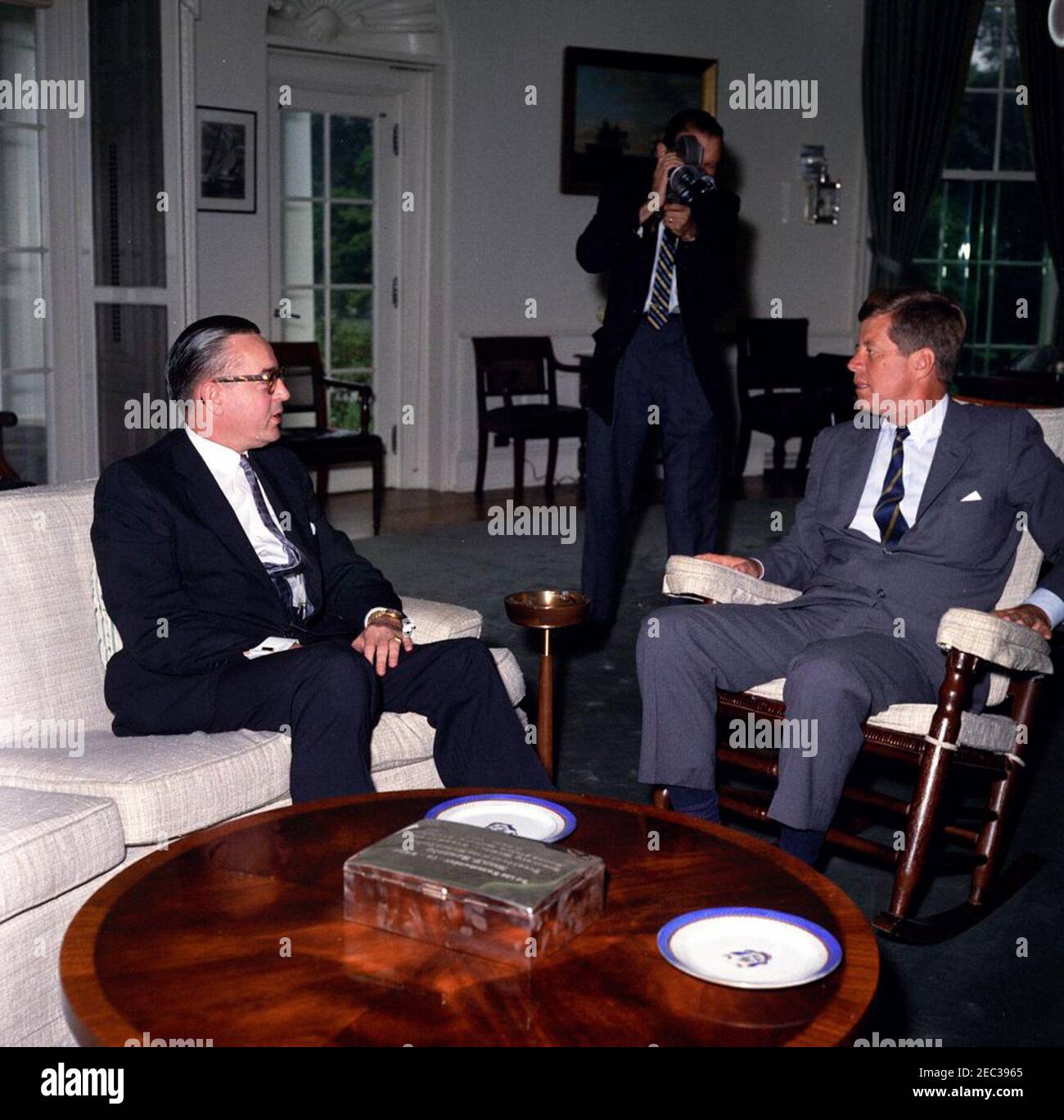 Treffen mit dem US-Botschafter im Sudan, William M. Rountree, 10:06am Uhr. Präsident John F. Kennedy (im Schaukelstuhl) trifft sich mit dem neu ernannten Botschafter der Vereinigten Staaten in der Republik Sudan, William M. Rountree. Ein nicht identifizierter Fotograf filmt das Treffen. Oval Office, White House, Washington, D.C. Stockfoto