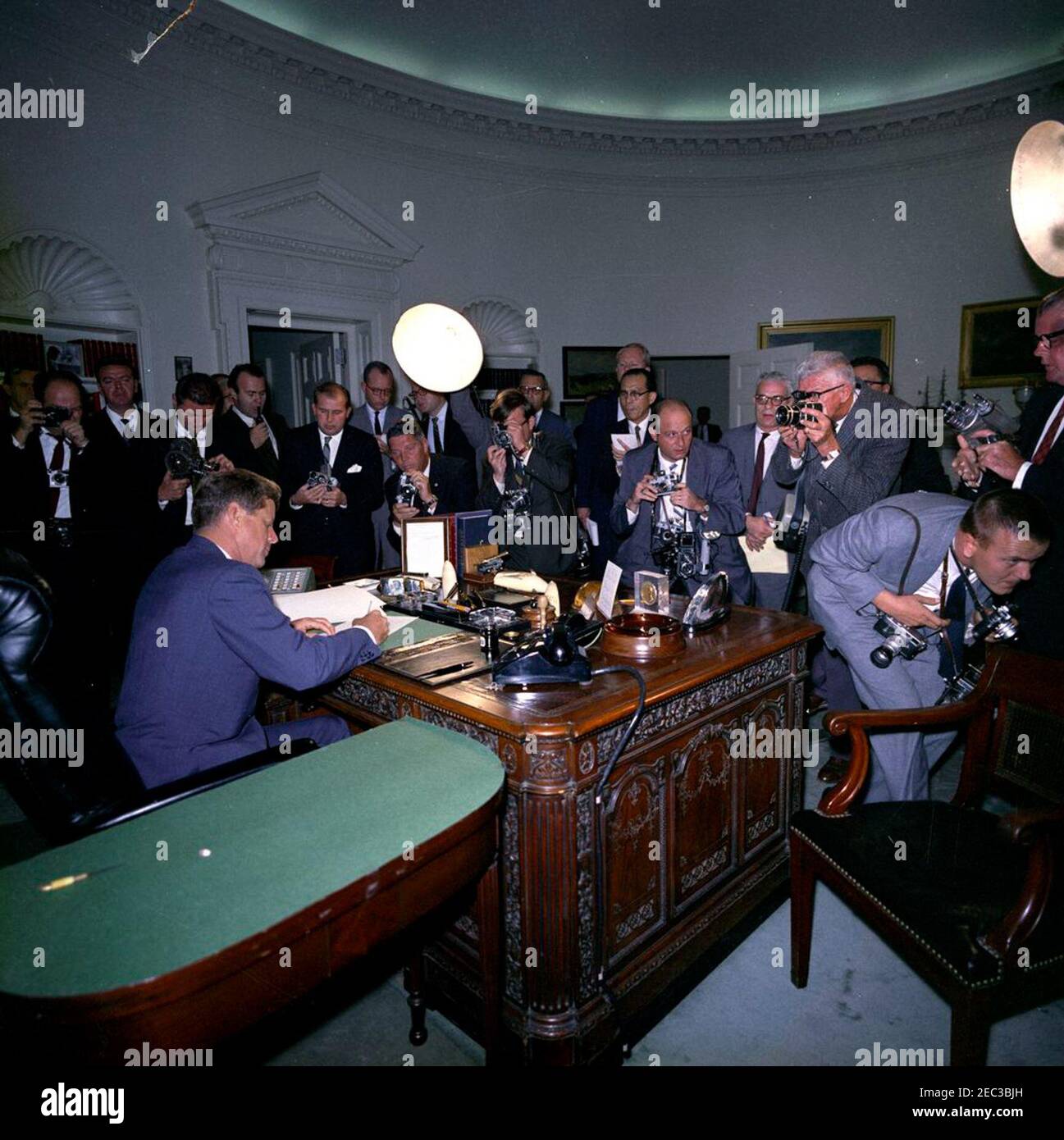 Unterzeichnung der Proklamation, Verbot der Lieferung von Angriffswaffen nach Kuba, 7:05pm. Präsident John F. Kennedy unterschreibt das Verbot der Lieferung offensiver Waffen an Kuba. Fotografen und Reporter beobachten. Zu den abgebildeten Personen gehören: Fotograf des Weißen Hauses, Kapitän Cecil Stoughton (Mitte links, über die Ecke des Schreibtisches gelehnt); Fotograf des National Park Service (NPS), Abbie Rowe (stehend an der rechten Ecke des Schreibtisches, Gesicht teilweise hinter der Kamera versteckt); Fotograf von United Press International (UPI), James K. W. Atherton (rechts, sich biegend). Oval Office, White House, Washington, Stockfoto Unterzeichnung der Proklamation, Verbot der Lieferung von Angriffswaffen nach Kuba, 7:05pm. Präsident John F. Kennedy unterschreibt das Verbot der Lieferung offensiver Waffen an Kuba. Fotografen und Reporter beobachten. Zu den abgebildeten Personen gehören: Fotograf des Weißen Hauses, Kapitän Cecil Stoughton (Mitte links, über die Ecke des Schreibtisches gelehnt); Fotograf des National Park Service (NPS), Abbie Rowe (stehend an der rechten Ecke des Schreibtisches, Gesicht teilweise hinter der Kamera versteckt); Fotograf von United Press International (UPI), James K. W. Atherton (rechts, sich biegend). Oval Office, White House, Washington, Stockfoto