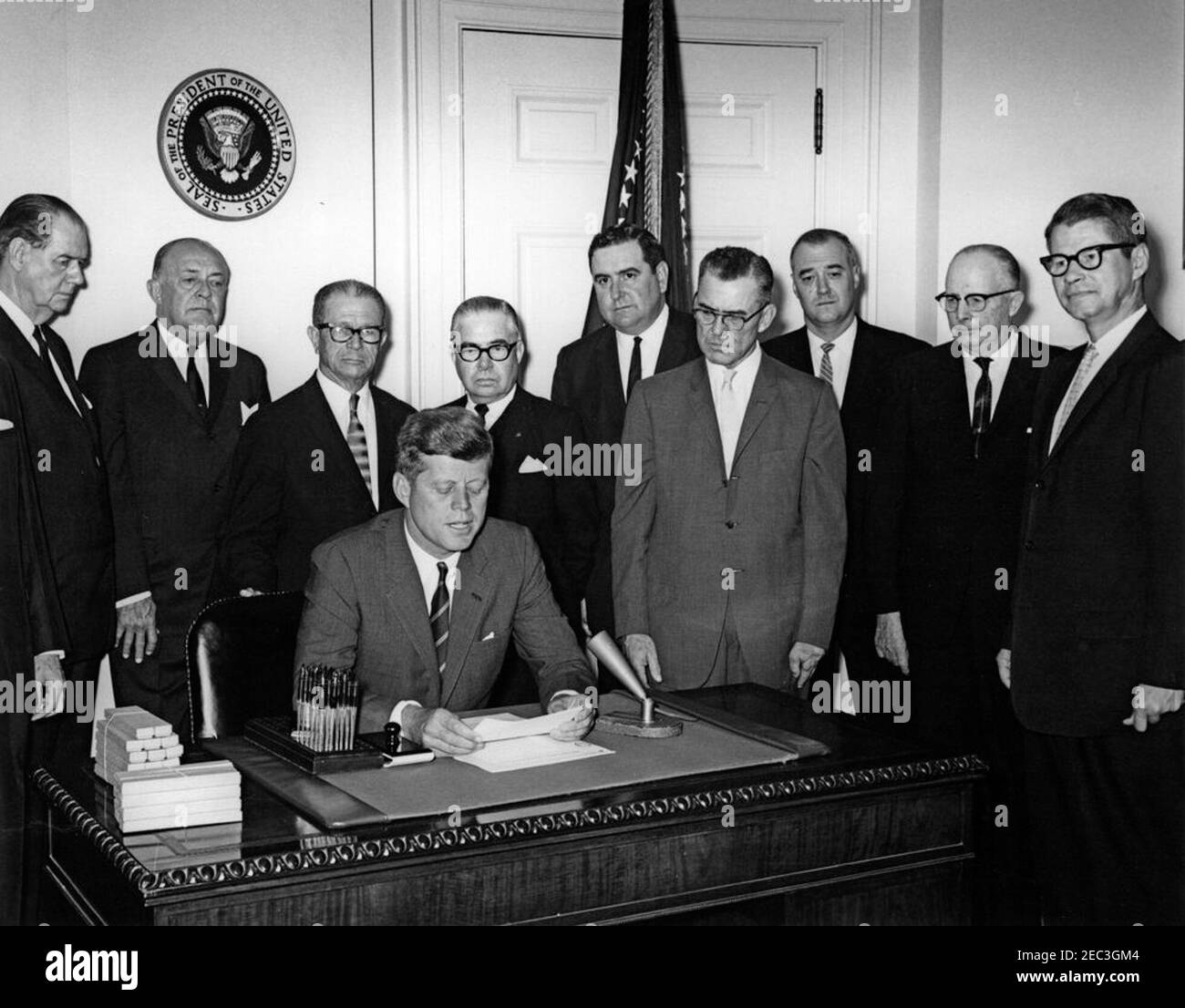 Bill Signing - H.R. 4997 Feed Grain Act, 12:35pm. Präsident John F. Kennedy (sitzt an der Rezeption) hält Bemerkungen zur Unterzeichnung des Feed Grain Act von 1963. Stehend (von links nach rechts): Senator Olin D. Johnston (South Carolina); Vertreter Harold D. Cooley (North Carolina); Senator Allen J. Ellender (Louisiana); Vertreter Paul C. Jones (Missouri); Präsident der National Farmers Organization, Oren Lee Staley; Glen J. Talbott von der National Farmers Union; Stellvertretender Administrator des Landwirtschaftsstabilisierungs- und Naturschutzdienstes (ASCS), Edwin A. u0022Edu0022 Jaenke; Geschäftsführer Stockfoto