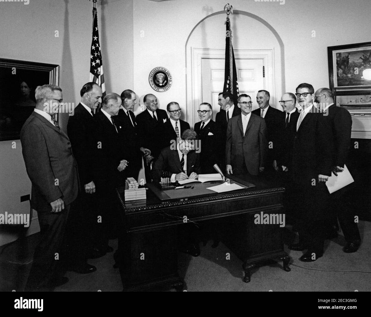 Bill Signing - H.R. 4997 Feed Grain Act, 12:35pm. Präsident John F. Kennedy (am Schreibtisch sitzend, lachend) unterzeichnet den Feed Grain Act von 1963. Stehend (von links nach rechts): Stellvertretender Landwirtschaftsminister, John P. Duncan, Jr.; Vertreter Graham Purcell (Texas); Vertreter W. R. Poage (Texas); Senator Olin D. Johnston (South Carolina); Vertreter Harold D. Cooley (North Carolina); Senator Allen J. Ellender (Louisiana); Vertreter Paul C. Jones (Missouri); Präsident der National Farmers Organization, Oren Lee Staley; Glen J. Talbott, der National Farmers Union; Associate Administr Stockfoto