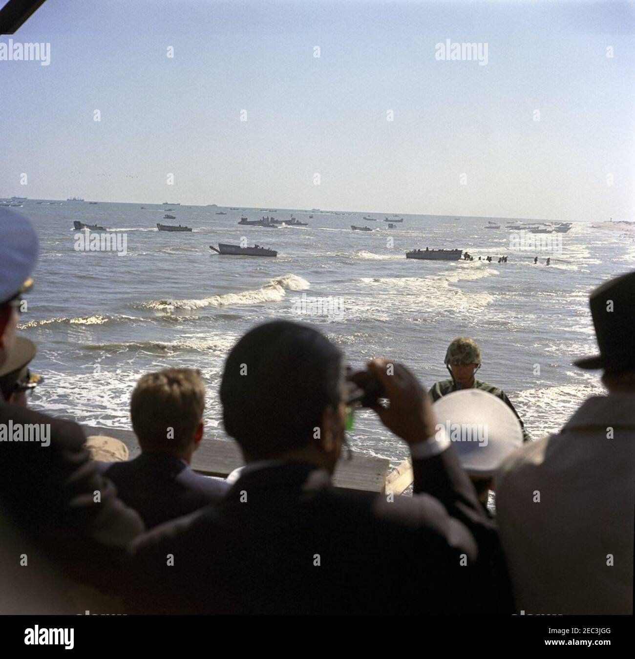 Besuch der Atlantikflotte: Präsident Kennedy sieht die Übungen des Marine Corps im Bogue Field und Onslow Beach, Camp Lejeune, North Carolina, 2:11pm Uhr. Präsident John F. Kennedy (unten links, zurück zur Kamera, mit Sonnenbrille) sieht sich eine Demonstration der amphibischen Landeoperationen der US-Marine und des Marine Corps am Onslow Beach vom Riseley Pier, Camp Lejeune, North Carolina, an. Stockfoto