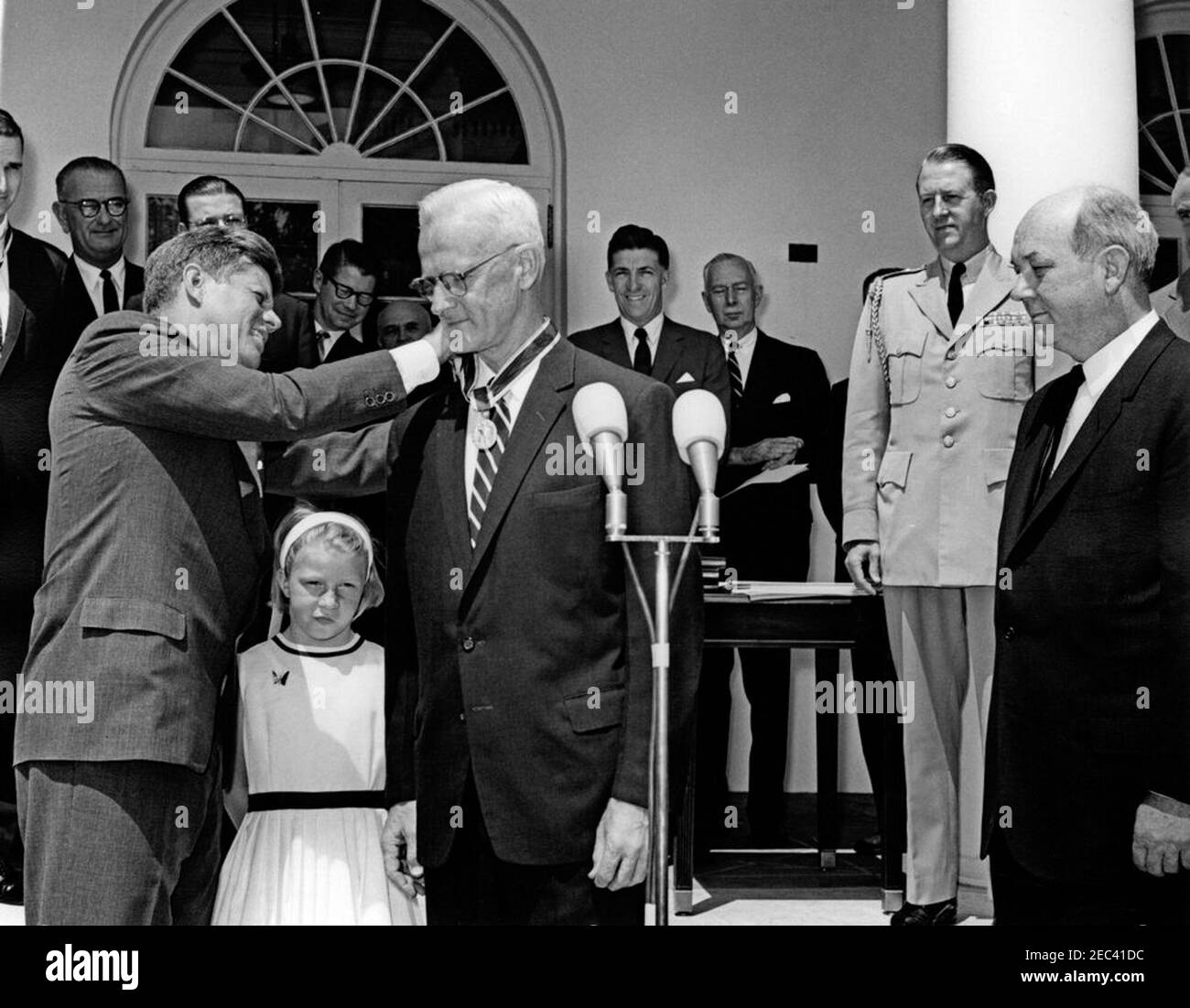 Verleihung der Distinguished Civilian Service Awards, 11:30am Uhr. Präsident John F. Kennedy überreicht den Preis Presidentu0027s für den Distinguished Federal Civilian Service an den stellvertretenden Kommandanten für auswärtige Angelegenheiten des National war College, Botschafter Winthrop G. Brown (Mitte, hinter Mikrofonen), bei einer Zeremonie im Rosengarten des Weißen Hauses, Washington, D.C. Anne Brown, Tochter von Botschafter Brown, Steht neben ihrem Vater; Staatssekretär Dean Rusk beobachtet rechts. Im Hintergrund (von links nach rechts): Preisträger und stellvertretender stellvertretender Verteidigungsminister für Syst Stockfoto