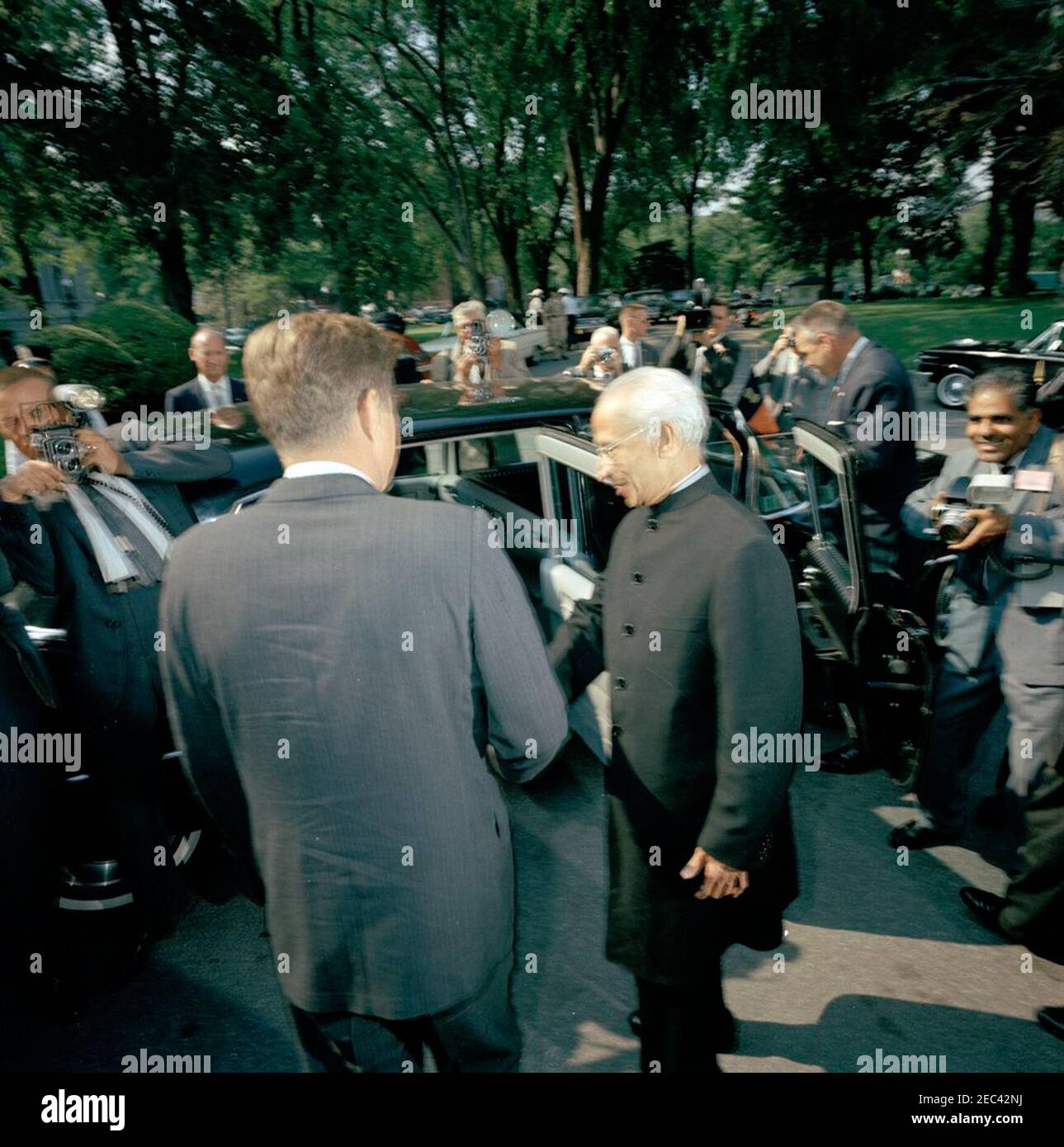 Abreise von Dr. Sarvepalli Radhakrishnan, Präsident von Indien, 4:40pm Uhr. Präsident John F. Kennedy schüttelt bei seiner Abreise aus dem Weißen Haus die Hände mit Präsident von Indien, Dr. Sarvepalli Radhakrishnan. Im Hintergrund (hinter dem Auto): US-Chef des Protokolls, Angier Biddle Duke (ganz links); National Park Service (NPS) Fotograf, Abbie Rowe (Mitte links). Alle anderen sind nicht identifiziert. Eingang im Westflügel, weißes Haus, Washington, D.C. Stockfoto