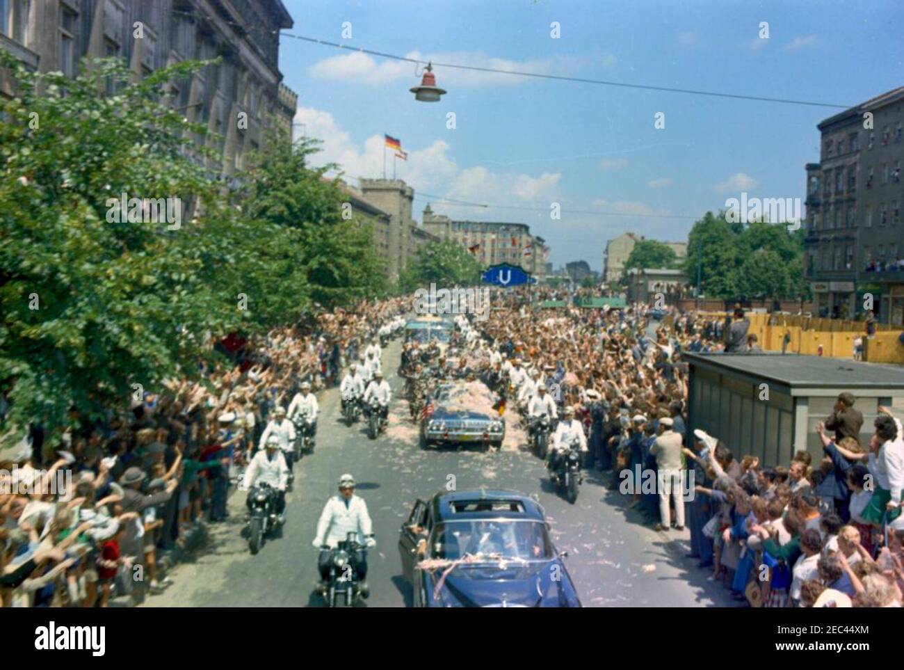 Europa-Reise: Deutschland, West-Berlin: Präsident Kennedy im Autokat mit Willie Brandt, Bürgermeisterin von West-Berlin, und Konrad Adenauer, Bundeskanzler von West-Deutschland. Präsident John F. Kennedy (im zweiten Auto) steht in der Präsidentenlimousine (Lincoln-Mercury Continental Cabrio), während seine Autokolonne durch West-Berlin, Westdeutschland (Bundesrepublik) reist. Mit dem Präsidenten: Bürgermeister von West-Berlin, Willy Brandt; Bundeskanzler Konrad Adenauer. Menschenmassen säumen die Straße und werfen Konfetti. Stockfoto