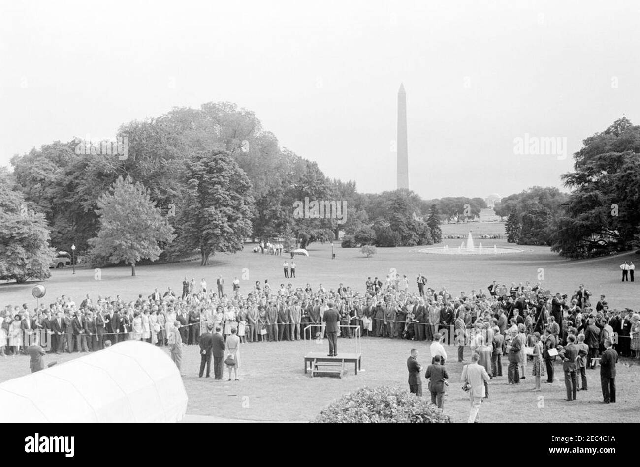 Besuch der Friedenskorps-Auszubildenden, 4:25pm Uhr. Präsident John F. Kennedy (im Vordergrund, auf der Plattform speakersu0027) hält eine Gruppe von Friedenskorps-Auszubildenden eine Rede. Ebenfalls im Bild: Stellvertretender Direktor für Programmentwicklung und Operationen des Friedenskorps, Warren W. Wiggins; Leiter der Abteilung für Ausbildung des Friedenskorps, Dr. Joseph F. Kauffman; Wochenschau-Fotograf für United Press Movietone, Thomas J. Craven, Sr.; Praktikant im Presseamt des Weißen Hauses, Mimi Beardsley; Fotograf des National Park Service (NPS), Abbie Rowe; Geheimagent des Weißen Hauses, Arthur L. u201cArtu201d Go Stockfoto