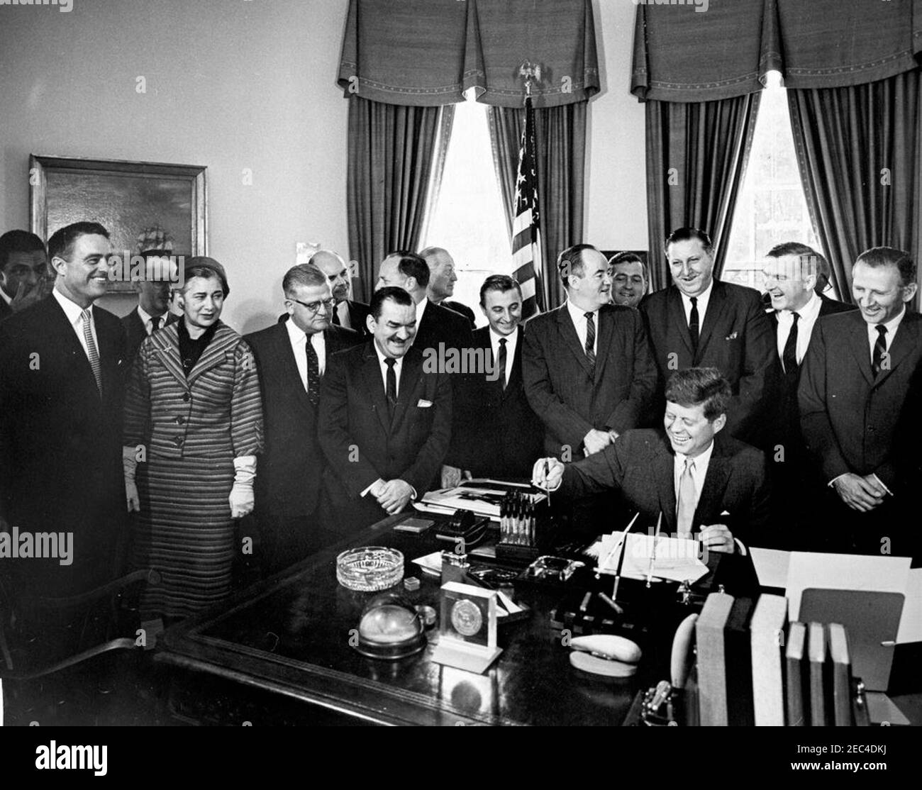 Bill Signing - H.R. 7500 Öffentliches Recht 87-293, Peace Corps Act, 9:45am. Präsident John F. Kennedy (lachend) unterzeichnet HR 7500, das Peace Corps Bill, im Oval Office, White House, Washington, D.C. mit Blick auf (L-R): Senator Claiborne Pell von Rhode Island (im Rücken); Direktor des Peace Corps, R. Sargent Shriver; Senator Philip A. Hart von Michigan (im Rücken); Vertreter Edna Kelly aus New York; Vertreter Chester Merrow aus New Hampshire; Vertreter Thomas F. Johnson aus Maryland (hinten); Vertreter Clement Zablocki aus Wisconsin; Vertreter Wayne L. Hays aus Ohio (teilweise verborgen Stockfoto