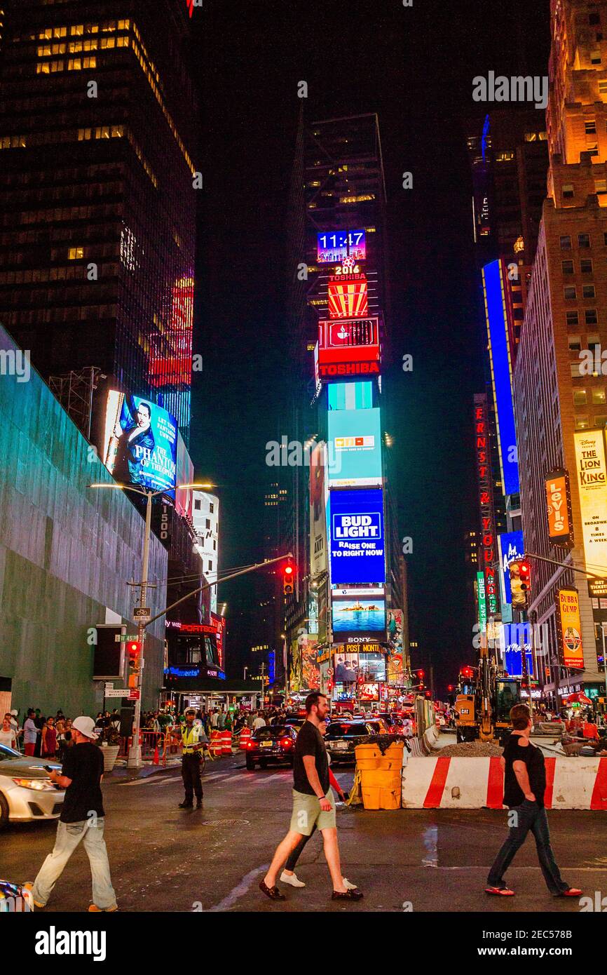 Nachtansicht des Times Square mit drei Personen, die die Straße überqueren Und Traffic-Agent, der den Datenverkehr verwaltet Stockfoto