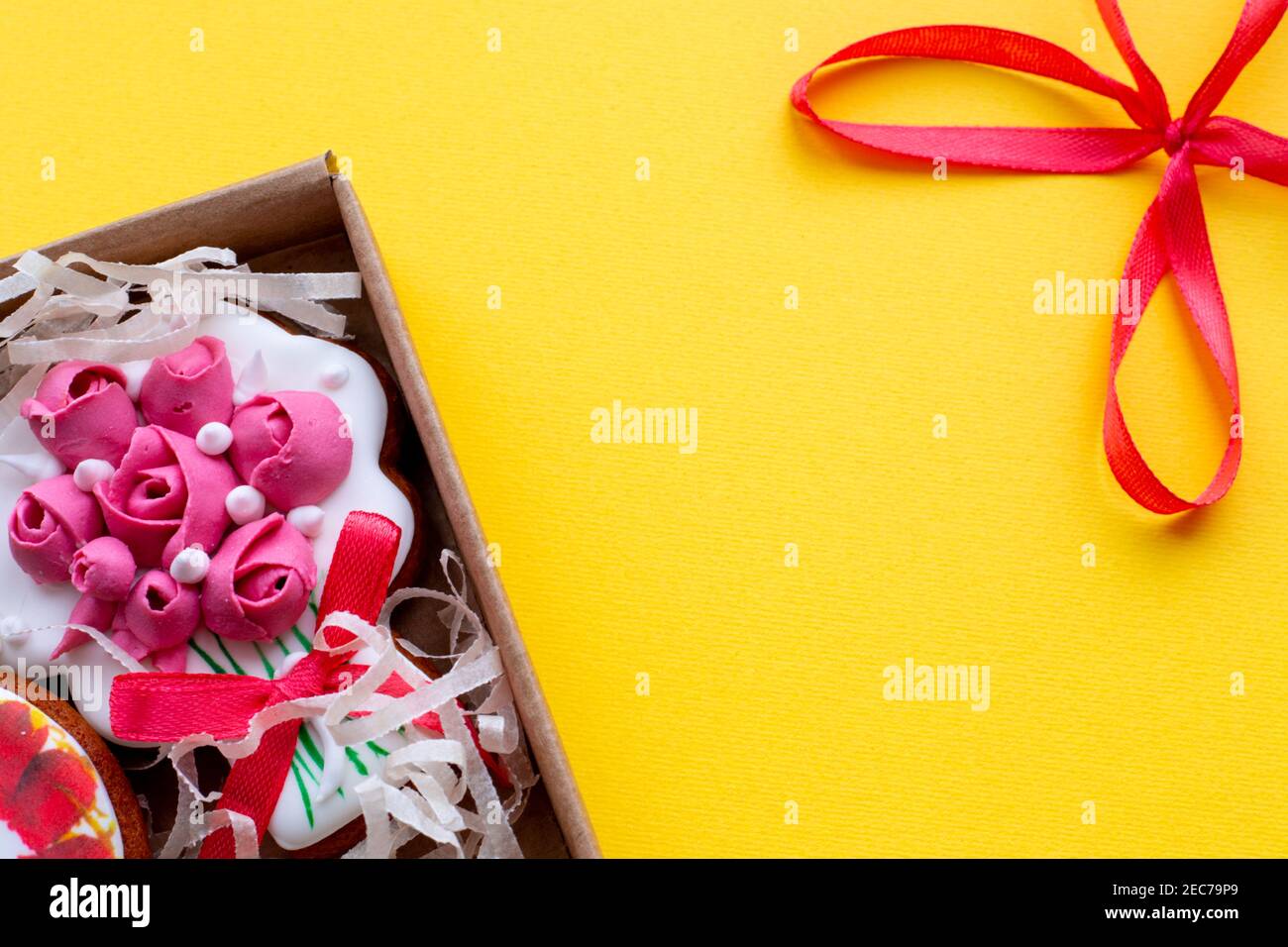 Gelber Hintergrund mit einer roten Schleife und einer Schachtel mit dekorativen Cookies, Vorlage für Text Stockfoto
