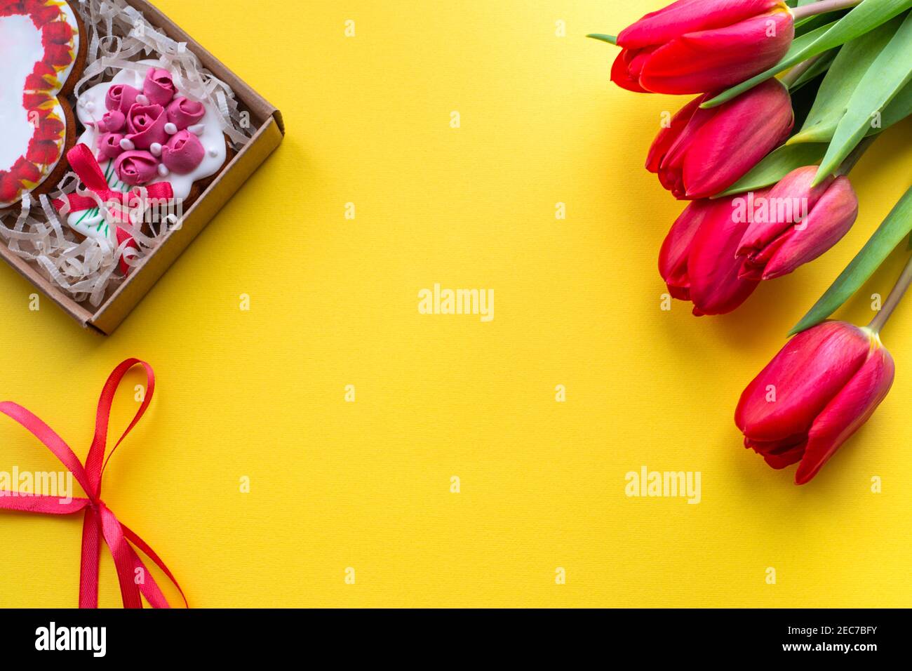 Gelber Hintergrund mit einer Box mit dekorativen Cookies und roten Tulpen, Vorlage für Text Stockfoto