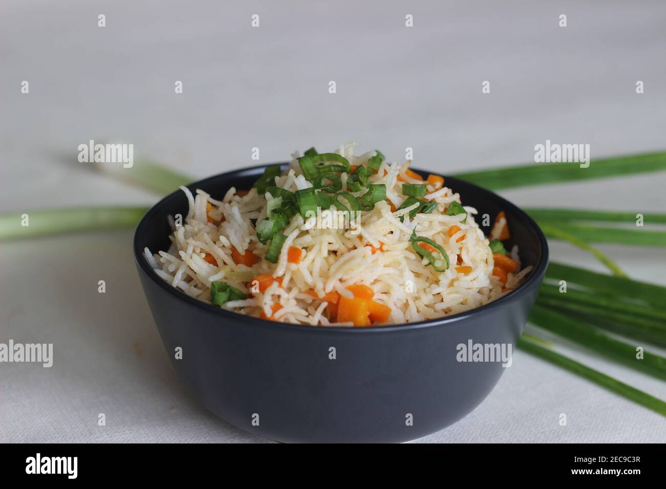 Gemüsekarotte gebratener Reis mit indischen Gewürzen. Schuss auf weißem Boden zusammen mit Karotten und Frühlingszwiebeln Stockfoto