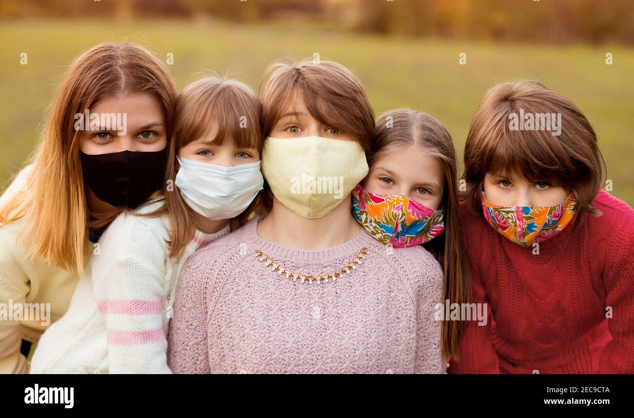 Die Gruppe der Kinder in den schützenden medizinischen Masken gehen durch Straße beim Herbstuntergang. Konzept Quarantäne Stockfoto