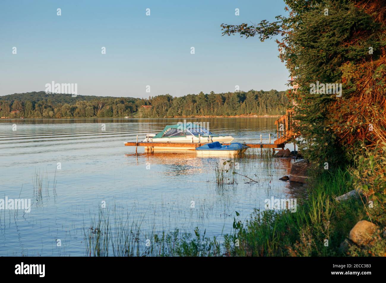 Sommer auf See Hütte. Kleines Jachtboot am hölzernen Dock Pier am See bei Sonnenuntergang. Canadian Ontario Muskoka Reise Ziel Ort. Wassersport im Sommer Stockfoto