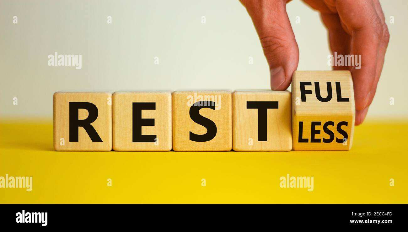 Symbol „Restless“ oder „RESTful“. Geschäftsmann dreht den Holzwürfel, ändert das Wort "stlos" in "stful". Schöner gelber Tisch, weißer Hintergrund, Polizist Stockfoto