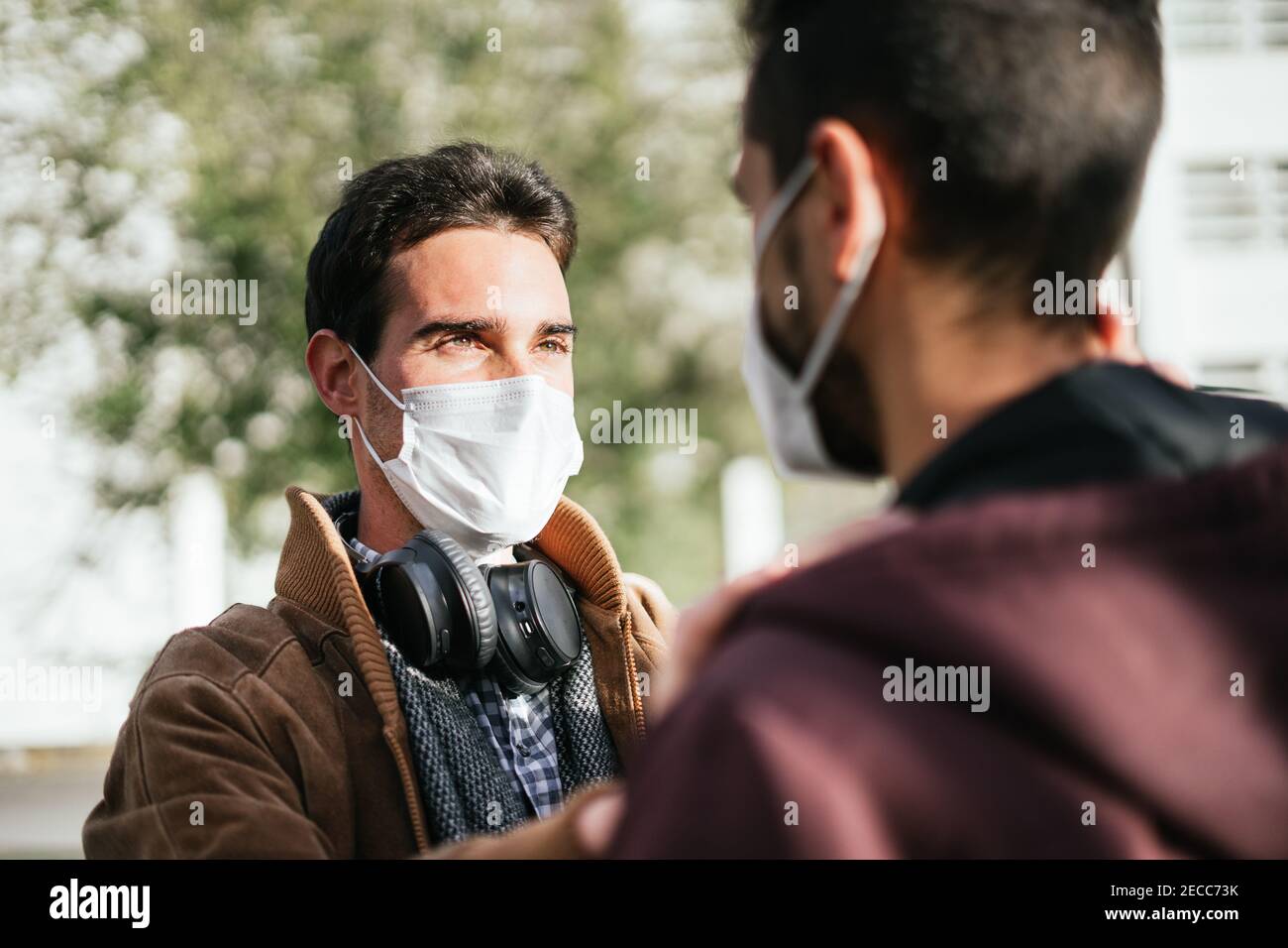 Zwei schwule Männer mit Gesichtsmasken, die sich liebevoll angusten, während der eine das Gesicht des anderen berührt. Stockfoto