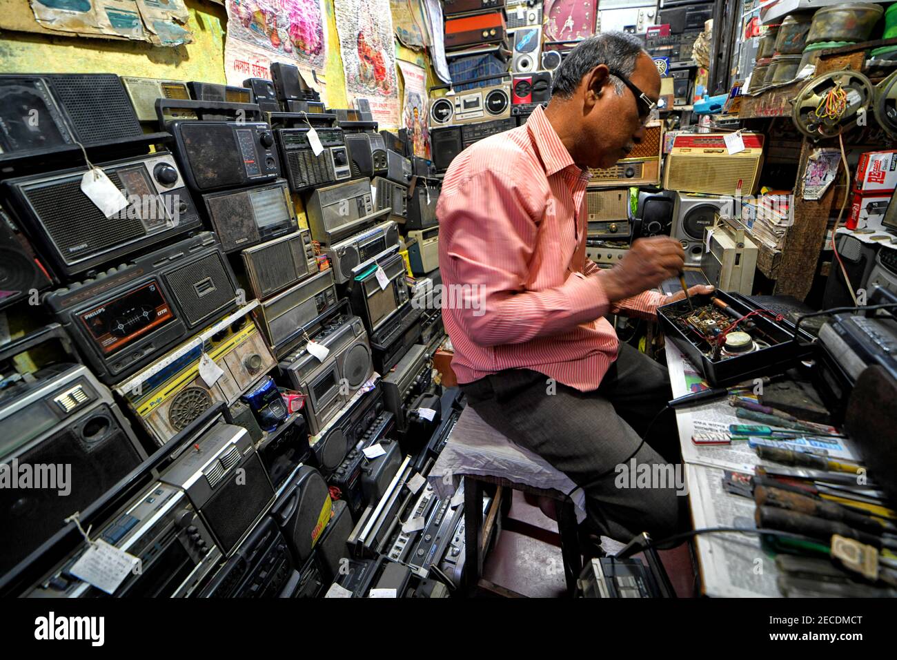 Ein Radiomechaniker sah in seiner Werkstatt arbeiten mit verschiedenen Arten von Radios umgeben.World Radio Day ist ein internationaler Tag gefeiert am 13. Februar jedes Jahr, wie von der UNESCO erklärt. Stockfoto