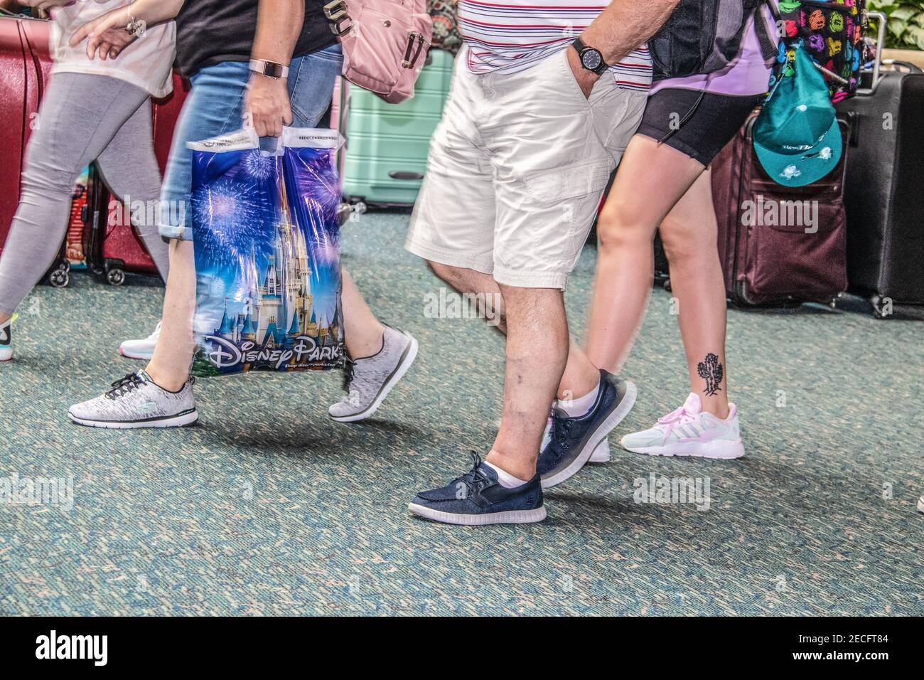 7- 13-2019 Orlando USA - Familien oder Paare zu Fuß Ein Flughafen, der mit einer Geschenktüte von Disney World zurückkehrt - Beschnitten mit Gepäck im Hintergrund Stockfoto