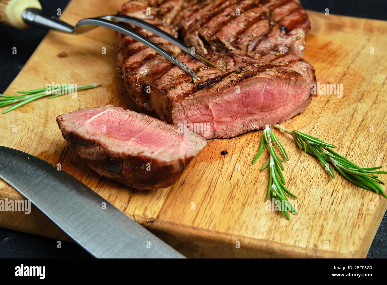 Nahaufnahme von saftigem Steak auf Holzschneidebrett Auf schwarzem Hintergrund Stockfoto