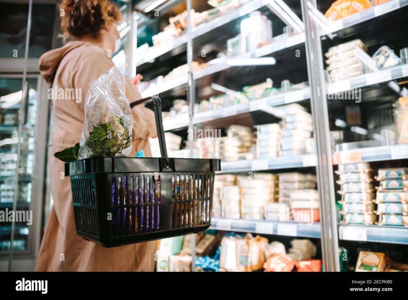 Frau, die einen Einkaufskorb hält und Lebensmittel im Regal betrachtet. Shopper einkaufen Lebensmittel im Supermarkt. Stockfoto