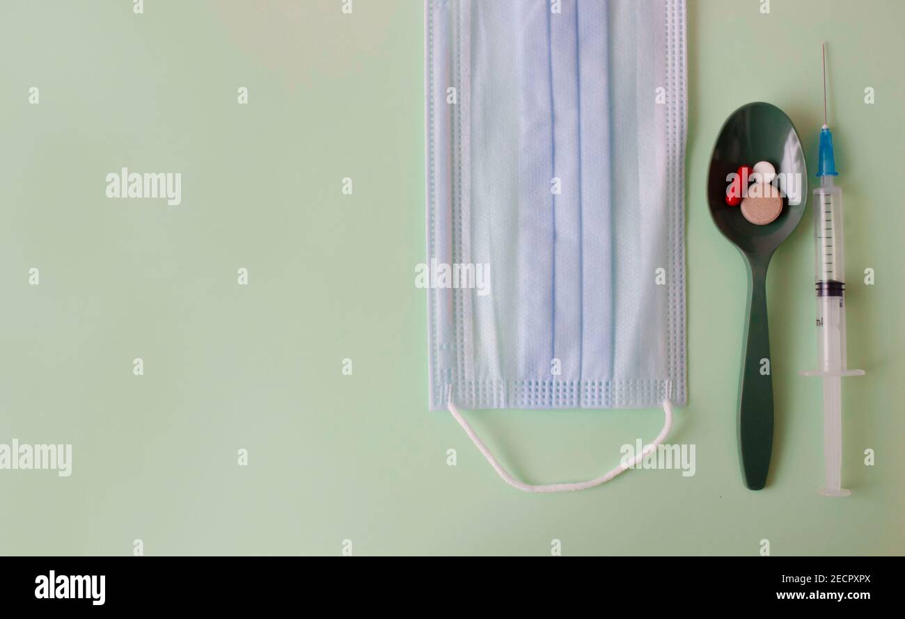 Ein grüner Löffel mit Tabletten, eine medizinische Maske und eine Spritze auf einem farbigen Hintergrund. Medizinisches Layout Stockfoto