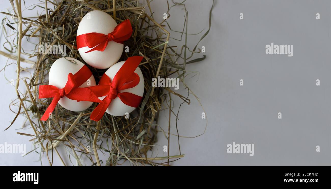 Drei Eier mit einem roten Bogen in einem Nest auf weißem Hintergrund. Osterkonzept Stockfoto