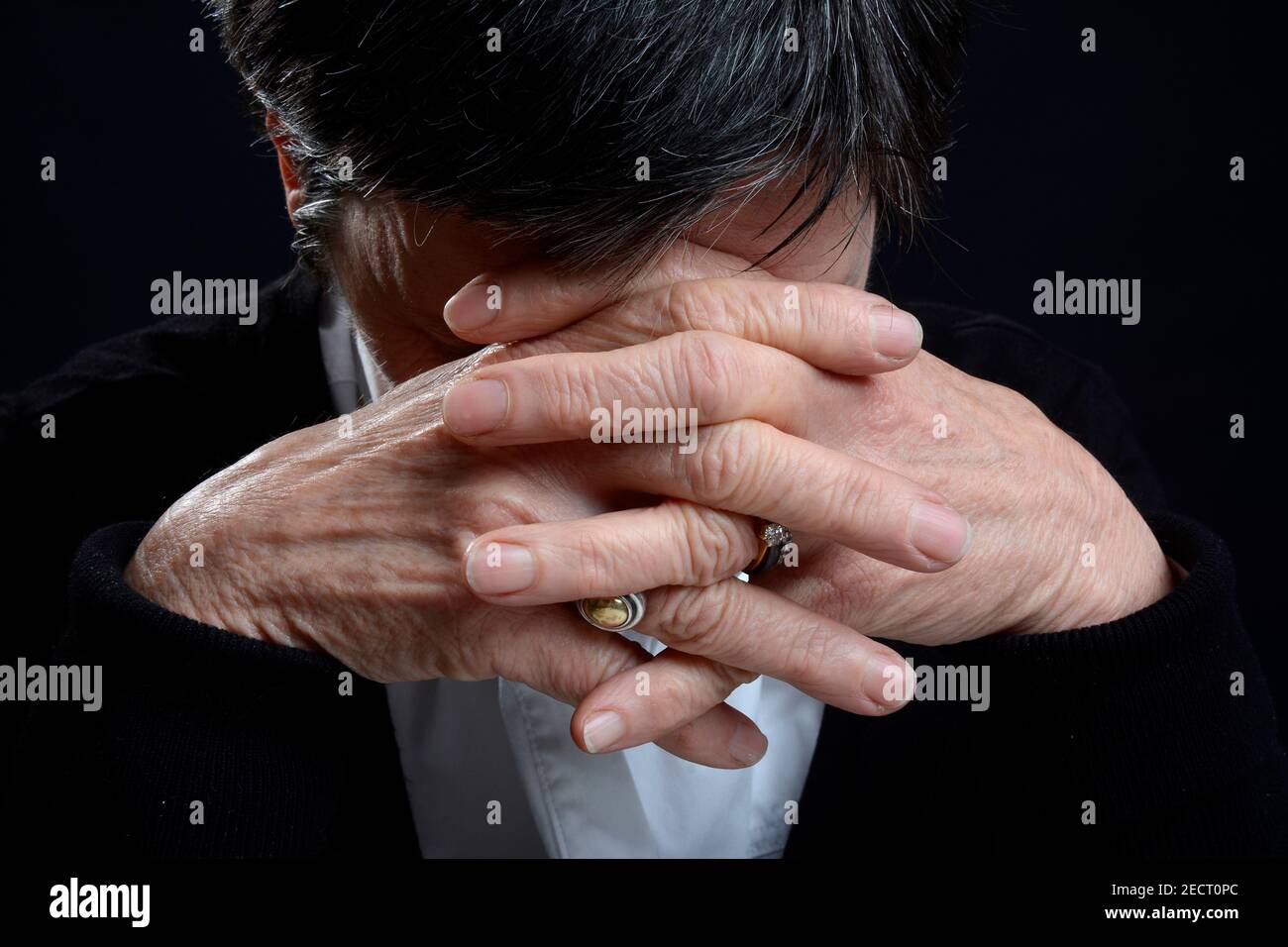 Emotionaler Ausdruck einer Person mit gebeugtem Kopf und geklammerten Händen in einem Moment der Besinnung oder Not Stockfoto