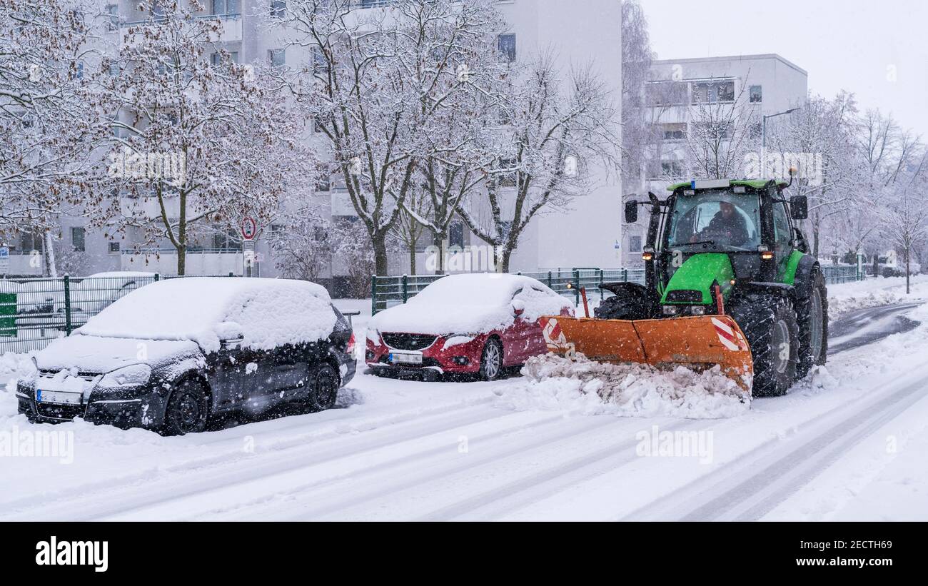 Ein Traktor mit einem Schneepflug räumt die Straßen in einem Stadt Stockfoto