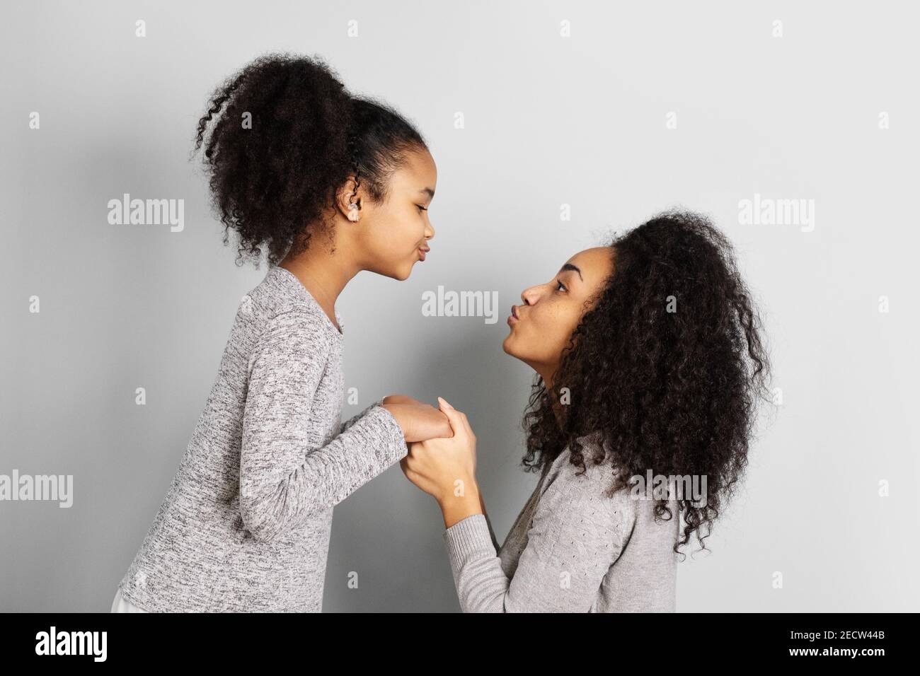 afroamerikanische Mutter mit ihrer Tochter, die sich isoliert auf neutralem grauen Hintergrund ansieht. Stockfoto